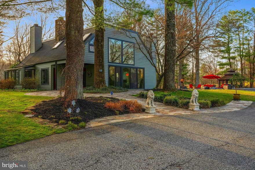 Set on a flat 3-acre lot, this home offers a lifestyle of leisure and relaxation, complete with an in-ground pool, tennis court, and lush greenery surrounded by woods for ultimate privacy. Manicured California-style grass enhances the resort-like setting—own the legacy of a home that perfectly blends luxury and privacy.

The contemporary residence showcases striking architectural design with geometric walls and patterns, complemented by dramatic floor-to-ceiling windows and doors that bring the outdoors in. The main level welcomes you with a breathtaking two-story living room featuring 20-foot ceilings, a geometric wood accent wall, and a wood-burning fireplace framed by expansive glass.

Flow seamlessly into the ultra-modern kitchen outfitted with UltraCraft cabinetry, a 7-foot waterfall island, stainless steel appliances, and elegant crystal chandelier pendants. The adjacent dining room, also adorned with a statement chandelier, invites you to dine while overlooking the serene greenery and stone patio with pool views.

The family room is a perfect retreat, offering another wood-burning fireplace, a designer accent wall, and panoramic views that wrap the space in natural beauty. The main level also includes three spacious bedrooms, two beautifully appointed bathrooms with marble mosaic floors and classic wall tile, and a private office.

Upstairs, the primary suite is a true sanctuary with soaring 10-foot ceilings, a flagstone fireplace mantel, and a luxurious spa-inspired bathroom featuring an oversized walk-in shower with dual showerheads, a deep soaking freestanding tub, and a large vanity.

The finished lower level expands the home’s lifestyle appeal with yet another inviting space for entertaining and everyday living. A full bar—complete with a dishwasher, refrigerator, and ample seating—anchors the space, flowing into a large family room perfect for gatherings. This level also offers incredible versatility with a spacious playroom, a dedicated gym, and a convenient half bath. In addition, a generously sized en-suite bedroom with its own full bathroom provides the ideal setup for guests, extended stays, or private accommodations.

The property also features a stylish guest house, ideally situated adjacent to the one-car garage—perfect for extended stays or private living quarters. This beautifully updated space offers a full modern kitchen with sleek flat-panel cabinetry, a waterfall-edge peninsula, and stainless steel appliances. Soaring ceilings and a cozy wood-burning stove create a warm yet contemporary feel, while the bright bedroom is framed by stunning windows that capture the surrounding greenery. Sliding glass doors in the living area invite in natural light and provide seamless indoor-outdoor flow, completing this thoughtfully designed and wonderfully modern retreat.

Countless updates enhance the home’s comfort and peace of mind, including a whole-house generator, new HVAC systems, a newly plastered in-ground pool, and more.

Ideally located with close proximity to Caves Valley Golf Club, as well as convenient access to major commuter routes, fine dining, and upscale shopping, this property offers both seclusion and accessibility.
