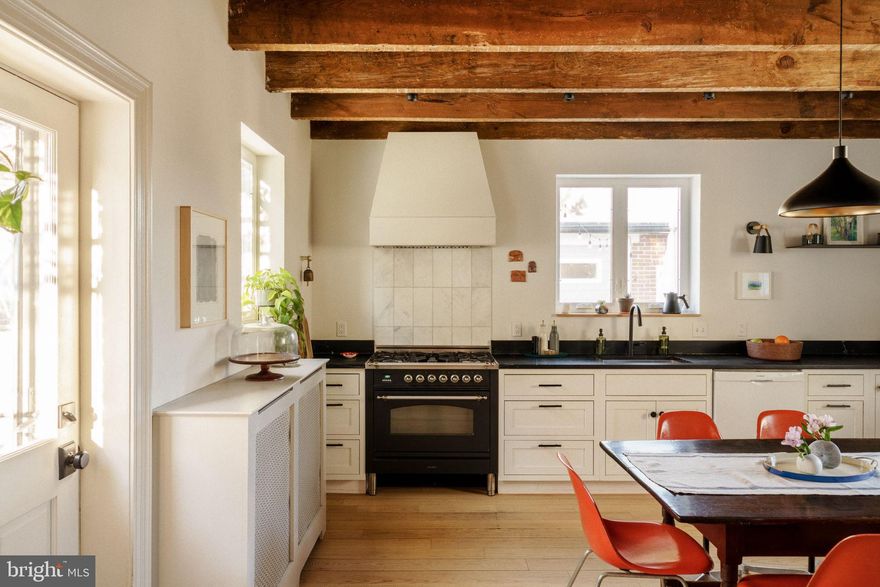 Perfectly positioned between Germantown Avenue and Pastorius Park — just one block in either direction — this restored Chestnut Hill home offers walkability to shops and restaurants, everyday access to green space, easy reach of the Wissahickon trails, and the added flexibility of a detached studio tucked just beyond the courtyard.

A stone single with a distinctive mansard roof, the home has been thoughtfully reworked with a clear design sensibility and consistent material choices throughout. Exposed rafters, deep-set windows, and layered materials give the home texture and warmth, while modern upgrades — updated systems, central air, and a reimagined kitchen and baths — support comfortable daily living.

You enter into the front parlor: floor-to-ceiling built-in shelving, a window seat, white oak floors that run through the entire first floor. Next is the bright, comfortable living room with a stylish ceiling fan and original millwork. Basement access is from this room. Through to the heart of the home — the kitchen: heavy timber beams overhead, soapstone counters, a professional-style range beneath a custom vent hood, structural floating shelves, and a dining area anchored by botanical wallpaper. A room that works as hard as it looks good. A side door connects directly to the driveway.

Throughout the home, lighting, paint choices, and built-ins added by the current owners reflect an intentional and cohesive approach to design.

Four bedrooms and two full baths span three levels, with every nook considered. The second-floor bath: freestanding soaking tub, zero-entry shower, heated marble floors, heated towel bars, matte black fixtures. The third-floor bath: a jack-and-jill between two bedrooms with a deep green tile shower and live-edge wood vanity shelf. The basement provides additional storage, laundry, and a powder room for everyday convenience.

Outside, a courtyard sits beneath a pergola that fills with Concord grape vines each summer — enjoyed as an outdoor dining and lounge area with the feel of a tucked-away European courtyard. Off-street parking for two cars adds everyday practicality.

Just beyond the courtyard sits a former three-car garage, now an approximately 500-square-foot artist's studio with additional storage.  Filled with natural light and equipped with its own mini-split heating and cooling system, it offers a rare layer of flexibility — studio, office, workshop, fitness space, guest overflow.

Set in the heart of Chestnut Hill, this is a home with a point of view — positioned for buyers who recognize what they're looking at.