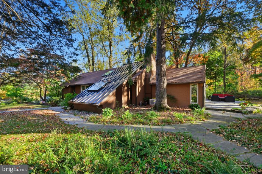 Nestled on a tranquil, tree-lined property, this inviting 3-bedroom, 2-bath ranch home offers the perfect blend of modern sophistication and relaxed country living. Thoughtfully designed with a contemporary influence, the home features an elegant open floor plan, soaring ceilings, and walls of glass that draw the outdoors in — creating a serene and light-filled living experience. A welcoming atrium entry introduces the home’s stylish interior, where architectural details and natural materials come together to create warmth and character. The main living area offers a wonderful sense of openness, connecting the living room, dining room, and kitchen in a seamless flow ideal for both entertaining and everyday living. The living room is anchored by a handsome fireplace and custom built-ins, while the dining area provides a charming spot to gather with family and friends. At the heart of the home, the chef-inspired kitchen impresses with its expansive wood-topped center island and counters, commercial-grade gas range, 2 oversized skylights that flood the space with natural light, and a generous pantry for storage. From here, access to the adjoining  screened porch makes indoor-outdoor living effortless. The family/great room addition is a true showpiece — surrounded by glass and framed by views of the lush, wooded landscape. With its warm wood-burning stove, pumpkin pine hardwood flooring and inviting design, it’s a perfect space for relaxing, reading, or simply enjoying the beauty of nature year-round. Hardwood floors enhance the main living areas, adding continuity and elegance throughout. The lower level offers incredible flexibility, featuring an additional bedroom, full bath, kitchenette, 2nd family room, study,  storage room and laundry/mechanical room. With its own private entrance, this versatile space is ideal for extended family, guests, or as a private suite for adult children. Outside, the grounds are nothing short of spectacular. Mature trees and natural landscaping create a sense of seclusion and peace. The in-ground pool with a gazebo invites summer fun, while the screened-in porch offer shaded havens for outdoor dining or quiet reflection. A bluestone terrace adds a touch of timeless sophistication, and the three-car carport provides ample parking and convenience. This beautiful home embodies the essence of a quiet country retreat, yet it remains just minutes from the best of Bucks County — including the shops and restaurants of New Hope, the charm of Peddler’s Village, excellent schools, parks, and major commuter routes. Whether as a full-time residence or a weekend escape, this property offers an unmatched combination of privacy, comfort, and connection to nature.