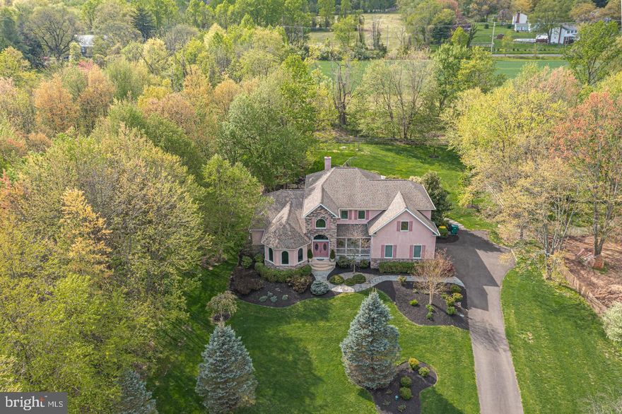 Custom built home with first floor primary suite in Central Bucks School District. Offering charm and hospitality, this manicured beauty has an acre of land and backs to open farm fields. The welcoming 2-story foyer showcases the home’s neutral decor, elegant moldings, rich hardwood floors, and open concept. A tray ceiling billiard or formal living room to the left of the entry showcases the views from its triple arched windows. Across the way, the column accented dining room is spacious and perfect for hosting large family gatherings and offers access to the cozy front covered porch thru a set of plantation shutter double doors. Continue the open layout to the vaulted family room where a dramatic floor to ceiling stone wood burning fireplace with gas starter is centered between a series of 4 large windows. The adjoining kitchen makes a statement all on its own with a striking architectural stovetop stone arch, granite countertops, custom cabinetry, walk-in pantry, stainless steel appliances including a Dacor oven, convection microwave, warming drawer and an eat-at-counter providing seating for three. The breakfast nook welcomes you with picturesque views thru its many windows overlooking the private, split rail fenced backyard with mature trees and a stone walled surround pool with magnificent hardscaping. A mahogany covered porch and roomy rear deck with hot tub ready capabilities provide additional exterior entertaining space. A convenient primary suite can be found off the family room offering a full bath with unique ceiling detail and dual vessel sinks, walk-in closet, sitting area with gas fireplace and access to the rear deck. Hardwood floors will be installed in early May. Completing this level is a laundry/mud room, coat closet, access to the 2-car garage and a half bath with rear yard access. Downstairs is unfinished and proposes endless possibilities for additional living space with its high ceilings. An office/bonus room and three additional bedrooms; one with its own full bath and the other two sharing a Jack and Jill full bath with two vanities, all with granite countertops and tile floors, complete the 2nd level with an overlook to the main level family room and front entry. Boasting endless comfort, this home is conveniently located close to downtown Doylestown for that quick commute to Philadelphia via train and the 295 corridor. Central Bucks Schools.