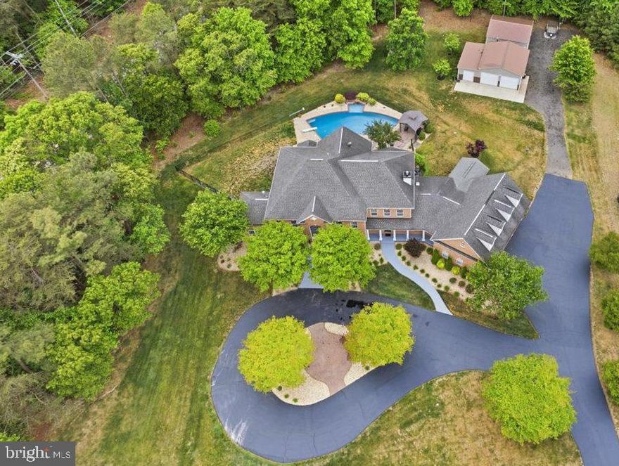 Luxury Multi-Generational Estate with Resort-Style Backyard + Extensive Workshop/Garage Space on 2 Private Acres
Welcome to this exceptional custom-built 8,600+ SF estate designed for multi-generational living, large-scale entertaining, and luxury everyday comfort in the heart of mid-Calvert County. Perfectly situated on 2 private acres, this one-of-a-kind brick-front property offers the ideal setup for extended family, in-laws, adult children, live-in care, au pair living, or long-term guests; all with flexible spaces that rarely come available in Southern Maryland.
Inside, the thoughtfully designed main level features a private in-law suite/guest wing with a separate entrance and screened porch, creating true independent living potential while still feeling connected to the home. The expansive floorplan includes a large eat-in kitchen, formal dining room, executive office with custom wood accent walls, spacious family room, and a stunning morning room with soaring 12-foot ceilings and marble flooring. Hardwood floors span most of the main level.
Upstairs, the luxurious owner’s retreat feels like a private sanctuary with tray ceilings, a fireplace, coffee bar, and spa-like proportions. Three additional oversized bedrooms and two full baths complete the upper level.
The fully finished walk-up lower level was built for entertaining and flexible living, featuring a second full kitchen, media room, billiards area, built-in entertainment space, a fourth fireplace, and a full bath with a tiled shower—ideal for pool access, guest overflow, or private lower-level living arrangements.
Step outside into your own private resort. The outdoor living space centers around a stunning 20'x40' heated pool with a tanning shelf, diving board, stone waterfall, and expansive patio spaces designed for unforgettable gatherings. Two oversized pavilions create the ultimate setup for outdoor entertaining, celebrations, cookouts, and summer weekends at home. A separate fenced pet area adds even more convenience.
For car enthusiasts, hobbyists, contractors, small business owners, or anyone needing serious storage and workspace, the property also includes two detached outbuildings with four additional garage bays, workshop space, water, electric, and slab foundations.
This is more than a home — it’s a rare opportunity to own a private family compound-style estate with luxury amenities, flexible living options, and unmatched entertaining potential.
Home warranty conveys.