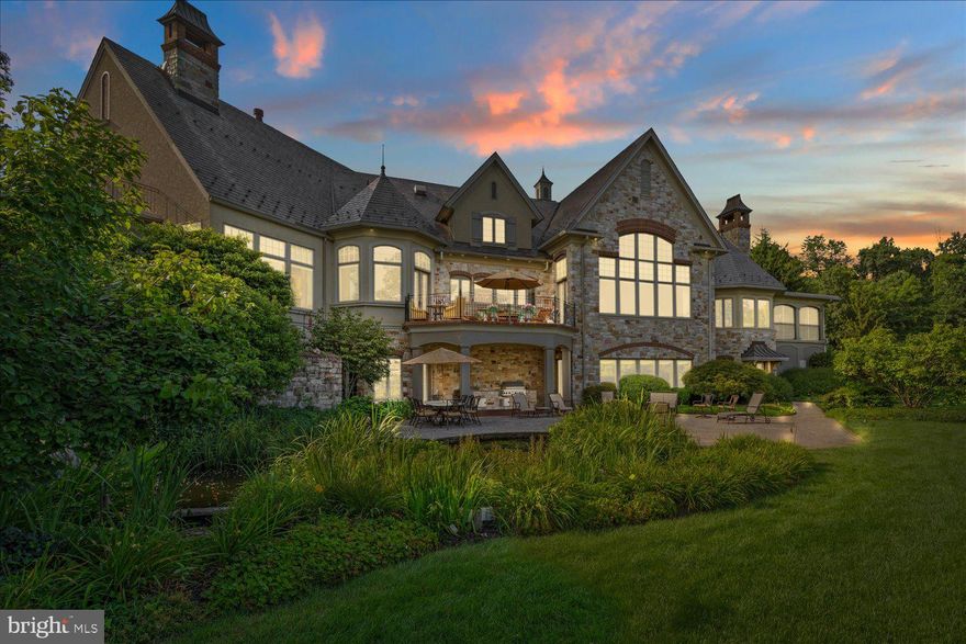 Nestled on a gorgeously manicured lot amid 10 secluded hilltop acres, this five-bedroom, 12,000+ sq-ft architectural masterpiece was lovingly designed by acclaimed architect Don Klinger to provide its owners supreme comfort and functionality while offering breathtaking views of the Susquehanna River Valley from nearly every room. With amenities too many to list (a sampling would include the five ensuite full baths plus four additional half-baths, the six fireplaces, and the 16,000-gallon outdoor koi pond with cascading waterfall), Hawkridge Estate takes mountain-side luxury living to a new level.
Situated at the end of a private, wooded drive within a gated community, the mansion features an all-natural stone façade and grey slate roof, with a spacious circular driveway and a broad double garage cleverly hidden to the side. The lofty entrance portico guides visitors into a stately hand-chiseled limestone foyer adorned with shimmering chandeliers and a sweeping, wooden grand staircase that curls upward to the second-floor bedrooms and a luxurious executive office suite.
Warm, sophisticated opulence characterizes every room of this three-story home, from the Great Room’s massive 24’-high beams and 1800-lb, no-seam rug imported from Thailand, to the elaborately hand carved millwork of the formal dining room. The expansive chef-quality kitchen features 200-year-old white oak floors, two-tiered solid granite counters, more than ample cabinet space, and a walk-in pantry. The regal owner’s retreat includes oversized closets and a jacuzzi surrounded by stained-glass windows. Hand-painted decorative tray ceilings throughout the house highlight natural motifs of plants, florals, and wildlife, elegantly complementing the house’s soothing earth-tone palette and Country French interior theme. The result is a retreat that is both luxuriously comfortable and hospitality ready.