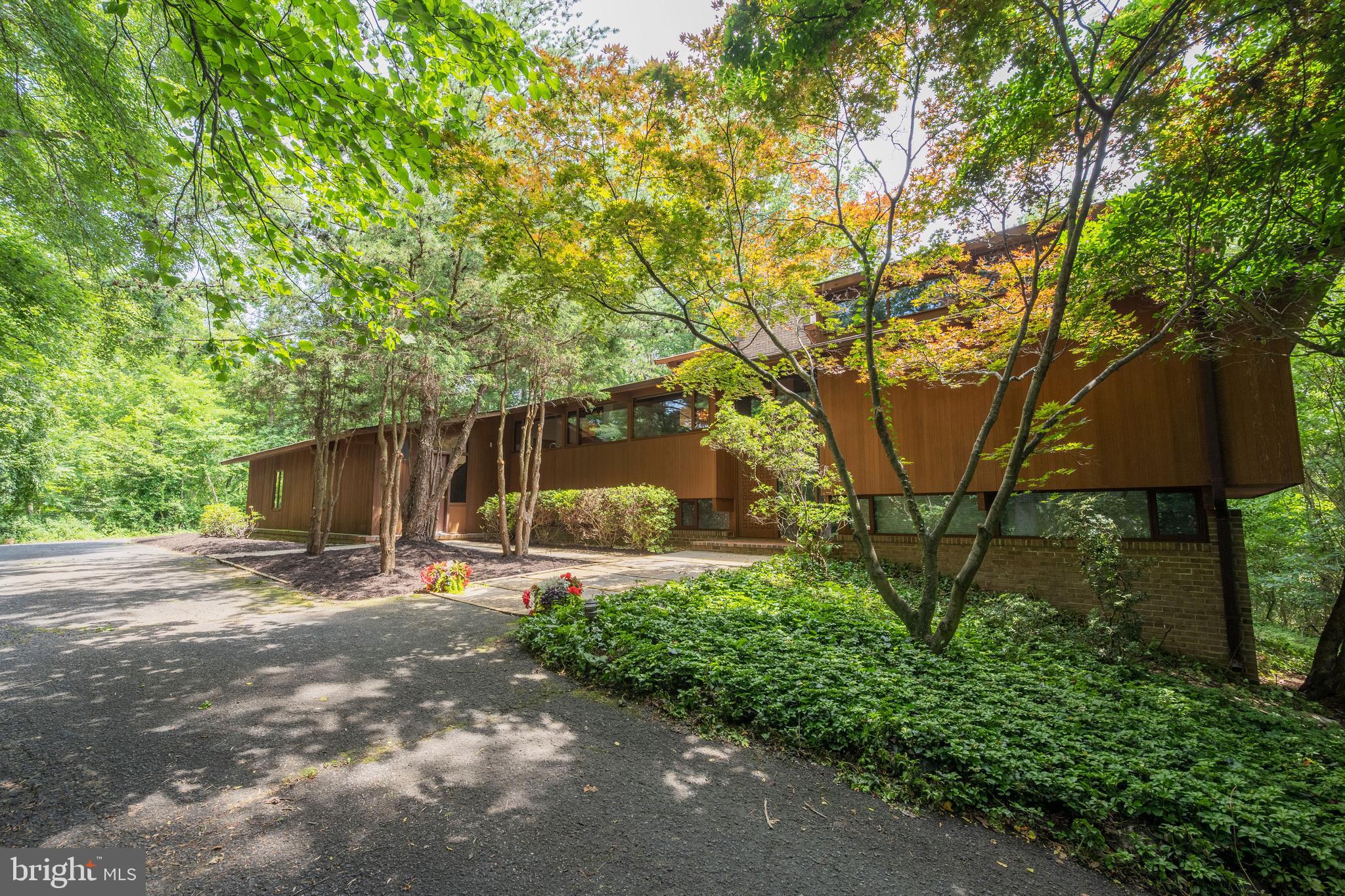 Nestled on nearly two private acres and surrounded by a canopy of mature trees, this architecturally intriguing mid-century modern deckhouse presents a rare opportunity to restore and reimagine a home of distinctive character and design. Striking wood-beamed cathedral ceilings and walls of glass define the main level, where expansive sliding doors and oversized windows bring the outdoors in. A dramatic floor-to-ceiling brick fireplace serves as a sculptural centerpiece between the living and dining rooms, framing serene, elevated views of the wooded landscape. The generous kitchen, complete with a center island, overlooks an impressive two-story solarium—an architectural showpiece bathed in natural light. Vaulted ceilings continue into the spacious primary suite, with soaring lines and potential for a true retreat. The walk-out lower level offers a versatile layout, including a large family room with wood stove, two additional bedrooms, a recreation room, laundry area, and direct access to the solarium. A second staircase leads to a practical mudroom and family entrance just off the attached garage. A deck off the main living area provides yet another space to enjoy the peaceful, tree-lined surroundings. With its striking lines, natural materials, and indoor-outdoor flow, this one-of-a-kind home is an inspiring canvas for modern living.
Langley High School, Cooper Middle School, Spring Hill Elementary School.