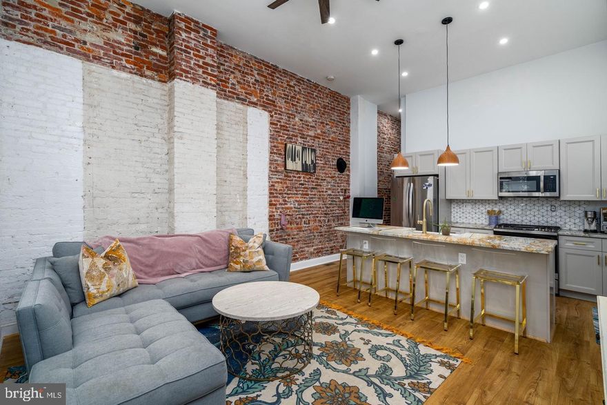 Sat across from picturesque Dickinson Sq Park, 1600 S 4th St #1 is a meticulously rehabbed single-level apartment teeming with luxury finishes and modern design. This corner unit offers 1 bed, 1 bath, a huge private patio, central a/c, and in-unit laundry. Soaring 13ft ceilings and beautiful hardwood floors frame the open living room and kitchen, anchored by an exposed brick wall. Tall windows at the front and side allow tons of natural light into the space. The stunning kitchen is fitted with shaker-style cabinets, stainless steel appliances, marble countertops, brass-toned hardware, and a geometric tile backsplash. There's also an island with seating, a farmhouse sink, and pendant lighting overhead. Off the kitchen, the exposed brick wall extends down a hall to the bright, airy bedroom suite, where you'll find towering windows, a custom exposed copper closet, and an LG laundry pair. A barn door opens to the luxurious, spa-like full bathroom adorned with designer tile throughout. Completing the unit is an expansive rear patio with lots of privacy and an entrance off the street. This outdoor space is waiting to be transformed into a garden oasis, perfect for hosting friends and family or relaxing with an evening glass of wine. Renovated in 2021, 1600 S 4th St #1's highlights include two keyless entryways, custom blinds, remote-controlled fans, and dimmable recessed lighting. In addition to everything inside, this fantastic location earns a WalkScore of 90! Lively Pennsport is overflowing with friendly local shops and popular restaurants, like Moonshine, Federal Donuts, Hermans, and The Dutchess. Whenever you want to spread out and get some fresh air, right across the street, sprawling Dickinson Square Park has benches, a playground, and a basketball court. It also hosts weekly farmer's markets every Sunday. Nearby shopping on Columbus Blvd includes Target, Acme, Wine & Spirits, Ikea, and Lowes. Plus, there's quick access to public transit, I-95, and South Jersey. Schedule your in-person or virtual showing today!