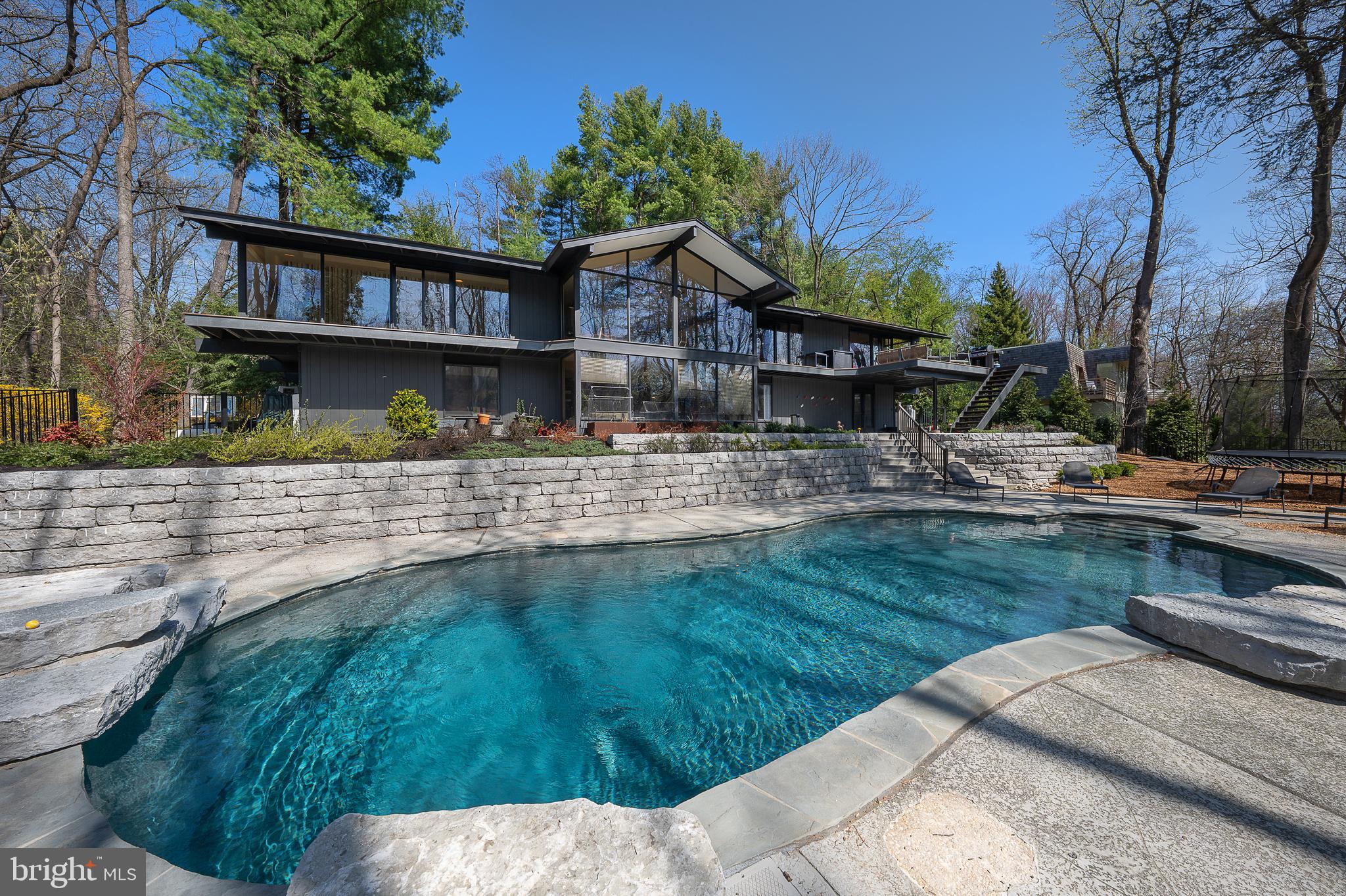 Tucked away at the end of a long, private drive and set on .82 acres of lush, meticulously maintained grounds, this stunning McElroy contemporary offers a rare blend of architectural drama, refined styling, and effortless livability. Designed by the renowned architect known for his “retreat styled” homes—elevated, glass-forward residences that blur the lines between sanctuary and everyday living—this home is a masterclass in form and function.
Built into the landscape and oriented for maximum enjoyment of the surrounding treetops, the home is defined by its signature use of large-format glass. Walls dissolve into windows, creating ever-changing views and making the natural world a living part of the home’s interior. From the moment you enter, you're greeted by a striking two-sided fireplace that anchors both the entry foyer and the central living/gathering space, setting the tone for a home that is both welcoming and quietly glamorous.
The open-concept main floor flows effortlessly through living, dining, and kitchen spaces, all smartly styled with a palette of organic materials and thoughtful textures. A chic green tiled backsplash in the kitchen plays beautifully against sealed wood service counters and a raised seating island that balances form with function. Flat prep space and excellent storage enhance the kitchen’s everyday utility, while a nearby study offers a moment of retreat within the openness. A stylish formal powder room completes the level.
The primary suite, also on the main level, is its own private haven. With treetop views, a spa-caliber bath featuring a soaking tub, standing shower, and a generous walk-in closet, the suite invites relaxation and renewal.
On the garden and pool level below, a spacious family room with additional gas fireplace, opens through sliding doors to the outdoors and seamlessly connects the interior living to the pool area. Three bedrooms—one with an en suite bath and two sharing a hall bath—offer flexibility for guests or family. A large laundry and service area serves both the pool and home, ideal for entertaining with ease.
Outside, a stylish breezeway with fire pit connects the main house to a two-car garage and offers yet another gathering space—perfect for evenings under the stars. With high-style finishes, intelligent design, and the rare feeling of complete privacy, this home is a singular expression of McElroy’s philosophy: refined, retreat-like architecture designed for the rhythms of everyday life.
Additional features you may not know: New wraparound rear deck and custom railings; Kitchen amenities include 2 ovens, 2 sinks, 2 refrigerators, 2 dishwashers; full laundry on garden/family level; Kitchenette with dishwasher on garden level; Primary bathroom / closet amenities include heated floors and full size washer / dryer.
