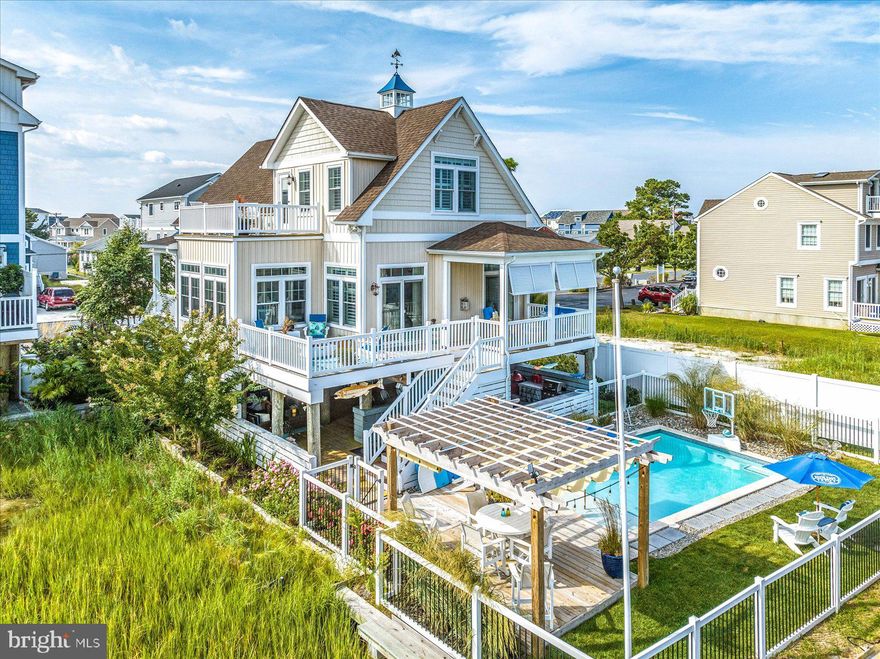 Luxury Coastal home, constructed by T & G Builders , featured in the Metropolitan magazine and was on the Sand Castle Tour of 2017! This home has an abundance of character and architectural details that only enhances the water vistas throughout the home. The central living space has a warm fireplace, hardwood floors, an open concept kitchen with custom cabinets,  a custom wood topped island with bar seating, large farmer sink with stunning gold faucet, custom pot filler over the stove and top-of-the-line appliances. Not to mention the dining area overlooking the canal all the way to Rt 90 Bridge! The main level has, what could be a main level suite, with attached bathroom and a stunning walk in shower.  Upstairs you'll find a second bedroom with custom builtin beds for your guests to enjoy.  Lastly, the third bedroom is also complete with an on suite bathroom,  a larger walk-in shower and gorgeous private balcony on the water.  Every room in this house is complete with a view!
Back on the main level a wide deck across the width of the house provides space for watching boats, sunbathing and dining area with a waterfront fire pit for a cozy gathering spot. The lower level is home to your own tavern including a handcrafted bar, table ideal for cracking crabs, outdoor tv and heated pool with a covered sitting area to watch this beautiful view.  You'll also find the  outdoor entertainment area for family parties, heated and air conditioned garage, bathroom and an outdoor shower to finish off this out door entertainment oasis!  Come sit in front of this custom beer can wall, swim in the outdoor heated pool on the canal or relax and watch the boats go by in your future home away from home.  All of this, comfortably nestled behind Harpoon Hannas and only a short jaunt away from Maryland and Delaware beaches including all the amenities North Ocean City has to offer! Make it yours today!