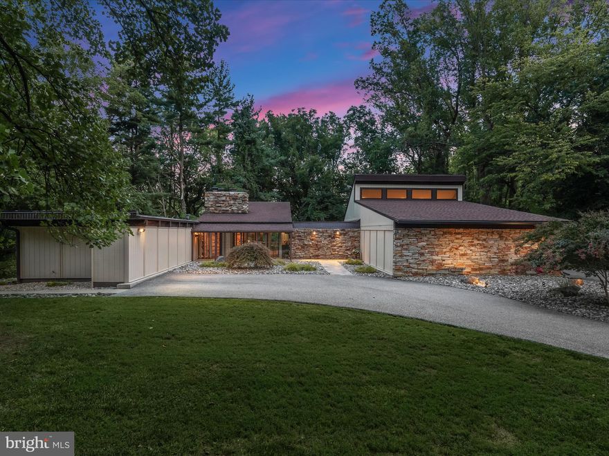 Introducing this absolutely stunning three-bedrooms, three-full and one-half bathroom Mid-Century Modern home, set on a serene 0.81-acre lot backing to lush woods. With over 4,300-square-foot spread across two levels, this home offers space for everyone with endless recent upgrades that blend luxury and convenience, complete with a new elevator installed in 2023. As you arrive, beautifully-maintained landscaping welcomes you, complete with outdoor lighting and stone walkways. Inside, you will be greeted by a grand foyer with a stacked stone wall, a vaulted ceiling, and a spiral staircase leading to the lower level. The main level boasts rich hardwood floors, exposed wood-beamed ceilings, and abundant natural light throughout. The living room is a highlight, showcasing a soaring vaulted ceiling, floor-to-ceiling glass wall overlooking the woods, and glass doors to access the rear deck. A stacked-stone wood-burning fireplace and wall cabinets with an audio hub complete this inviting space. The dining room, with its built-in cabinets and pass-through window to the kitchen, also opens to the rear deck for easy entertaining. Prepare your favorite meals in the gourmet kitchen that features stainless steel appliances, Ukrainian Volga Blue Granite countertops, a glass tile backsplash, and modern cabinets with pull-out drawers and under-cabinet lighting. Glass doors lead to a side deck, perfect for grilling or dining outdoors. The home's layout ensures ample storage, with a long hallway lined with closets and contemporary picture lights. The full bathroom on this side of the home features luxurious marble tile, a separate vanity area, and a tub-shower. Down the hall, the second and third bedrooms offer oversized windows and double closets. Moving to the other side of the home, the cozy den is another versatile space and includes elevator access to the lower level, a glass door to the deck and a newly-added ethernet cable. The half bathroom off the den is adorned with marble tile. An addition in 2017 expanded the home with an impressive primary bedroom suite and an oversized two-car garage, both recently updated with a brand new roof in 2024. The primary bedroom suite showcases a soaring vaulted ceiling, one wall of closets, and a large walk-in closet with custom California Closets systems. The luxurious ensuite bathroom features Italian Carrara marble, a BainUltra jetted tub with a new motor, a massive walk-in frameless shower with dual shower heads and a bench, and a dual sink vanity. Completing this side of the home is a closet with stacked laundry and access to the oversized two-car garage with 9-foot wide doors and extra storage space. Downstairs, the fully-finished lower level is perfect for entertaining or as an extended guest suite, with a newly remodeled bathroom that adds a walk-in shower, along with a new vanity and mirror. The level also includes a family room with quarry stone flooring, a stacked-stone wood-burning fireplace, floor-to-ceiling windows and glass doors to the rear yard. The family room also offers a wet bar with a granite countertop and the elevator. The recreation room, with porcelain tile flooring, offers ample space for everyone and could serve as a bedroom or lounge to make this a private living suite from the rest of the home on the main level. Additionally, the lower level includes extensive storage and a second laundry area with new washer and dryer. Thoughtful features further enhance this home with a three-zoned energy-efficient heating and cooling systems, central air conditioning with units updated in 2019 and 2020, and both oil and electric heat. Two water heaters, one replaced in 2020, ensure comfort for everyone. The crawl space houses the oil tank and a brand-new sewage ejection pump, adding to the home's extensive list of updates and modern amenities.