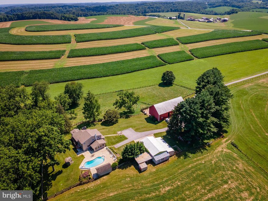 Over 93 acres of breathtaking, preserved Carroll County farmland can be yours at 2424 Shiloh Rd. Find complete seclusion while being minutes from downtown Westminster and the heart of Hampstead. With over 40 tillable acres, over 25 in pasture, and over 20 acres in woods, the land is a phenomenal mix of crop, field, and forest. The long, tree lined driveway pulls you in from the road, creating a sense of relaxation hard to ignore. The farm amenities include a large bank barn in great condition with concrete floor, stall/run in space, storage, and access to multiple smaller fenced fields. A 2 car garage includes an additional bay off the side for tractor parking or storage, concrete floor, large woodworking shop, loft storage space and additional room in the back. The custom farm house is spacious with beautiful hardwood floors throughout. A large living room with stone fireplace overlooks the barn. The eat-in kitchen has amazing storage, a center island, gas range, and enough table space for a full dining room table, including a walk out to the back deck and slider entrance to the screened porch that you'll never want to leave, offering peaceful moments overlooking your private land. The primary suite is on the main floor, with three closets, access to the full bath with updated shower, and a slider door to the back yard. An additional sitting room or family room, and office or play room with direct access to the backyard complete the first floor. There is plenty of available space - and configuration - to add another bedroom. Upstairs, find 2 large bedrooms with double closets - previously converted from 3 bedrooms to 2. There is an additional full bath with tub/shower combination upstairs. The basement is mostly finished, with another custom stone fireplace and walkout to the side yard under the screen porch. In addition to the family room or office space, there is a large storage and utility room, laundry room, and canning room in the lower level as well. The home has been lovingly and meticulously maintained over the years and it shows - it is one of those homes where you FEEL at home. The fenced back yard is stunning with a panoramic surround of fields and woods. The in ground pool, pool house, and gazebo provide opportunity for hours - or forever seasons - of outdoor fun. The farm at 2424 Shiloh is thriving and cannot wait to welcome its next occupants with stunning views, meticulously kept amenities, perfect spaces, and opportunities to grow in the ways only farmland and living outside just as much as inside can cultivate.