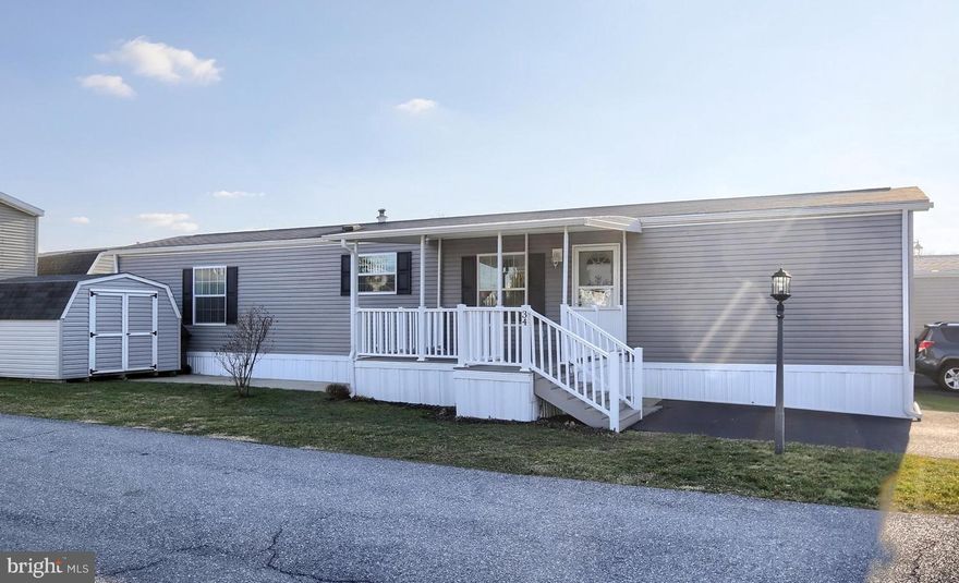 This newer home  is in excellent condition, low-maintenance, and ready for you to move right in! It is located on a corner lot  of a quiet, well-maintained community - enjoy relaxing on the large, covered deck overlooking the expansive green lawn across the drive! The home comes fully furnished with newer, modern furnishings (most Ashley & Bob's Furniture) and all appliances stay. Beautiful kitchen with white cabinets and lots of storage is open to dining area and living room. There is a laundry room with washer & dryer, cabinets and pull-out drawers in pantry cabinet. The first bedroom is a primary suite with walk-in closet and full bathroom en-suite with walk-in shower. The second bedroom is on the opposite side of the house for privacy. Second full bathroom has a tub shower and is accessed from the hallway, convenient for guests. There is also a large shed in great condition providing lots of storage. 55+ Community - buyers must apply for park approval. This home is move-in ready!