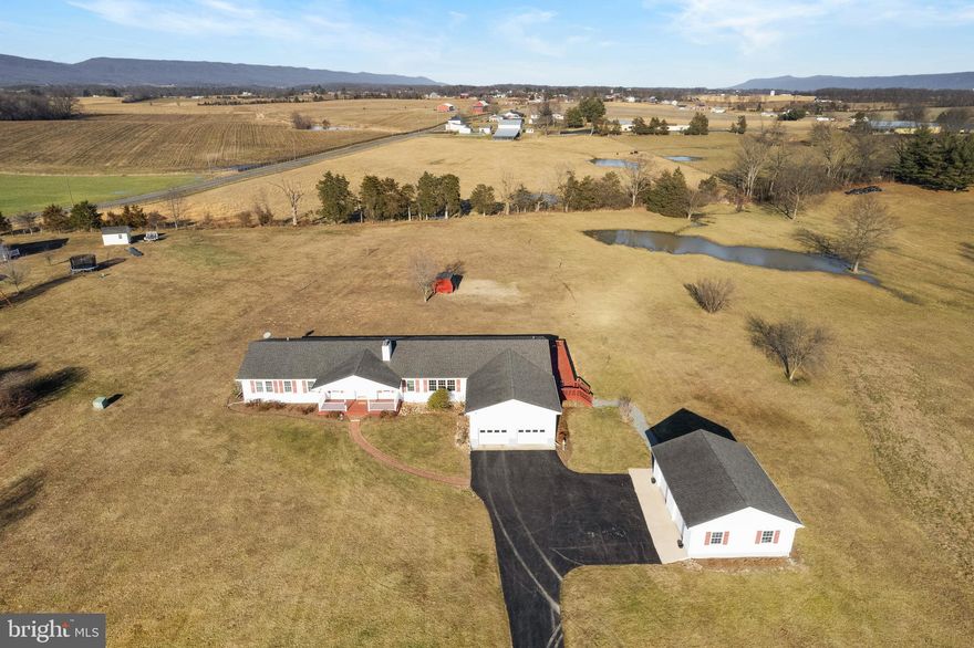 Experience the charm of comfortable country living in this beautiful 3,300 sq. ft. rambler situated on over 3 acres in Edinburg, VA. This home offers the convenience of one-level living and features a large farmhouse-style kitchen, perfect for gatherings with family and friends.  An attached 2-car garage, plus a large additional separate 2-car garage with electricity, provide ample space for vehicles and projects. Enjoy breathtaking sunsets from the front porch and stunning sunrises from the wrap-around deck at the back of the home. Recent 2024 updates include a new dishwasher, pressure tanks, HVAC and furnaces, kitchen sink and faucets, and an encapsulated crawl space.  This home is primed for many years of worry-free living. Discover what it truly means to relax and unwind in the tranquility of Edinburg, surrounded by scenic beauty and modern comforts.