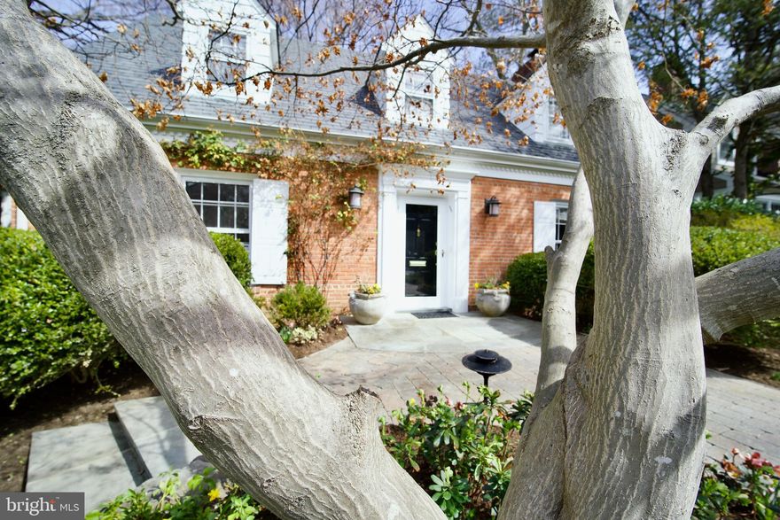 Nestled in the forest of The National Park Pinehurst Tributary, this stunning home is on the market for only the second time since 1956. It has been thoughtfully renovated by its current owners, including an addition by Hamilton Snowber Architects and Mauck Zantzinger Builders, which showcases breathtaking forest views and eastern light. Interior design by Zoe Feldman, featured in Architectural Digest, creates inviting spaces that are both intimate and welcoming. Landscaping and hardscaping by Fritz & Gignoux has transformed the gardens into a seasonal paradise, featuring a storybook front garden and a flat rear lawn surrounded by blooming garden beds and native trees. In the adjacent park, a tranquil tributary flows through a canopy of majestic tulip poplars and oaks, with hiking paths along the peaceful stream.
A winding stone path leads to the entrance of the brick colonial home, accentuated by large, imported English stone planters and crowned with climbing pink roses. Flowering dogwoods and vibrant azaleas create a stunning spring display. The screened-in porch offers breathtaking views and delightful birdsong, perfect for morning coffee. Natural light fills the home, and the property is complemented by low-voltage illumination at night. Four fireplaces enhance its charm, with the living room fireplace inviting cozy gatherings and seamless flow to the porch through French doors. The kitchen features a striking 12-foot island, a dining table accommodating eight, and stairs leading to the backyard. A unique saltwater fish tank and a wall of windows highlights the family room, while additional amenities include a Butler’s pantry, walk-in coat closet and a dry bar with engraved copper wall tiles.
The elegant dining room features a telescoping mahogany table that accommodates twelve (most furniture is for sale), complemented by a magnificent chandelier and rich silk drapes. The main-floor bedroom suite, currently an office, overlooks lush gardens and is ideal for guests. Upstairs, two additional bedrooms share a hall bathroom. There is ample storage and an attic fan providing natural cooling. The private primary suite features custom closets, built-in bookshelves, a romantic fireplace, and a luxurious spa-like bath with radiant heat flooring.
The renovated English basement includes an Au Pair/MIL suite, a spacious art studio with backyard access, and a recreation room with a wood-burning fireplace. There is a newly renovated table tennis room with French doors, and a laundry room and utility space. The backyard boasts a private stone terrace with an Italianate fountain—perfect for entertaining. Additional features include a whole-property irrigation system, path lighting, a wooden shed for refuse/recycling, and an Invisible Fence for dogs. 
Located in Barnaby Woods, Chevy Chase, DC, this tranquil sanctuary is just a short drive from Bethesda and downtown Washington, offering easy access to world-class dining and services.