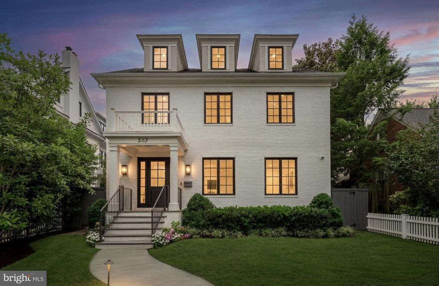 Set against the iconic backdrop of the National Cathedral in the heart of verdant Cathedral Heights, 3117 38th Street NW is a masterfully crafted modern farmhouse designed by GTM Architects in collaboration with MMg Development and built by Murillo/Malnati Homes. This distinguished team partnered with acclaimed landscape designer Lila Fendrick to deliver a residence that marries high design with luxurious livability, showcasing top-tier craftsmanship, seamless indoor-outdoor flow, and enduring style.

Completed in 2019, the home spans nearly 8,000 finished square feet across four thoughtfully designed levels. A white brick façade, black-trimmed windows, flagstone walkways, and manicured landscaping create timeless curb appeal. The front portico opens to a gracious foyer with sightlines that extend to the rear terrace, setting a tone of openness and elegance. Crown moldings, gleaming hardwood floors, and abundant natural light provide a sophisticated yet welcoming atmosphere.

The formal living room, with a gas fireplace and custom built-ins, overlooks the front garden. A tray ceiling and wainscoting in the adjacent dining room elevate formal gatherings. A marble-clad butler’s pantry with a beverage fridge connects seamlessly to the chef’s kitchen, which features custom stacked cabinetry, Wolf and Sub-Zero appliances, a full-height marble herringbone backsplash, and an expansive island with bar seating.

The open-concept kitchen and adjoining family room serve as the heart of the home. Coffered ceilings, a marble fireplace, and dual sets of French doors open to a flagstone terrace beneath a full-width pergola, perfect for indoor-outdoor entertaining and framed by views of the Cathedral.
Additional main-level features include a custom mudroom with built-in cubbies and side entry, access to a detached two-car garage with EV hookup, and a large walk-in pantry. A powder room and elevator complete this level.

Upstairs, the primary suite occupies its own wing and includes a private rear deck with cathedral views. The spa-inspired primary bath features radiant heated marble floors, a freestanding soaking tub, a glass-enclosed shower, a wall-spanning double vanity, and a private water closet. A custom dressing room with golden backlit shelving and abundant storage completes the suite. Three additional bedrooms, one currently used as a home office, share two full bathrooms along with a large, fully equipped laundry room.

The third level offers flexible living with two additional bedrooms, one styled as a game room with alcove seating, and a full bath. This space is ideal for guests, teens, or creative pursuits.

The finished lower level includes high ceilings, a recreation room with integrated Sonos sound, a wet bar with a Sub-Zero beverage fridge, a custom wine room, a fitness studio, a powder room, and a second laundry area. A private guest or au pair suite features a kitchenette, bedroom, and full bath.

Smart home systems include Legrand lighting, Honeywell Pro Series thermostats, integrated security with cameras and motion sensors, and multiple wall-mounted iPads for controlling lighting, sound, and surveillance.

Outdoors, a flat, professionally landscaped lawn is pool-ready and features a built-in grilling station, an extensive stone terrace, ambient lighting, irrigation, and French drainage systems for year-round enjoyment.
Steps from Massachusetts and Wisconsin Avenues, this premier location offers proximity to top-rated schools, lush parkland, and downtown DC. Elegant yet approachable, richly appointed yet supremely functional, 3117 38th Street NW is a rare offering that defines modern luxury living in Washington.
