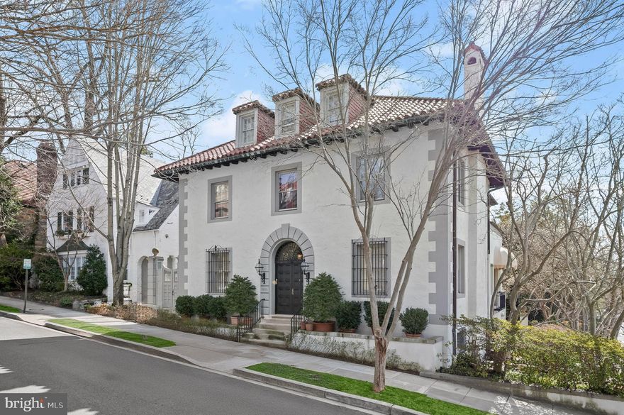 Nestled in the prestigious Kalorama neighborhood, 2330 Tracy Pl NW is a breathtaking Mediterranean Revival residence that epitomizes elegance, grandeur, and architectural refinement. Built in 1923, this stately four-level residence  showcases the craftsmanship of a bygone era while offering modern comforts for refined living. The home’s hand-troweled stucco and stone façade, quoined corners, arched entryways, and terracotta roof tiles create a striking first impression. Its handsome wood-paneled doors lead into the vestibule, where intricate ironwork and arched glass French doors open to a magnificent Entrance Hall wrapped in hand-troweled stucco walls and gleaming marble floors—an exquisite introduction to the home’s unparalleled classic elegance.

Designed for both grand entertaining and intimate gatherings, the main level offers beautifully proportioned formal rooms. The elegant living room boasts soaring ceilings, an exquisite stone fireplace, and decorative millwork, all illuminated by large windows and a stately crystal chandelier.  A sunlit sitting area, framed by arched Palladian windows and French doors, opens to a seating area on the balcony overlooking the rear yard, offering a view of the verdant lawn, mature trees and manicured plantings.

The formal dining room exudes timeless sophistication. Floor-to-ceiling French doors invite the outdoors into every dining experience by giving guests direct access to an extensive balcony overlooking the rear yard and courtyard beneath its arched loggias below.  A second ornate stone fireplace anchors the room, creating warmth and a perfect setting for unforgettable evenings.  

The gourmet kitchen is beautifully appointed with professional-grade Thermador, Sub-Zero, and Viking appliances, glass-front cabinetry, and a wine refrigerator. A butler’s pantry off of the formal dining room provides additional preparation space, ensuring effortless entertaining. A powder room and a coat closet are discreetly positioned nearby, preserving the main level’s refined aesthetic without compromising convenience.

The grand staircase leads to the upper living quarters, where the owner’s suite spans nearly the entire second level. This suite includes an expansive dressing room, a large walk-in closet, and a spa-like en-suite bathroom complete with a jetted soaking tub, dual vanities, bidet and standing shower with seating. The bedroom boasts a magnificent fireplace and opens to a spacious sitting room. An additional bedroom and full bathroom complete this second level. The next level up offers an additional well-proportioned bedroom, a den or sitting room, two full bathrooms, and built-in storage, providing privacy and comfort for family and guests alike. The lower level features an office, a full bath, a spacious laundry room, ample storage, and a two-car garage.  

Surrounded by embassies, ambassadorial residences, and some of the city’s most architecturally significant homes, 2330 Tracy Pl NW offers a distinguished setting just moments from Dupont Circle, Woodley Park, Georgetown, and Rock Creek Park. This exceptional home is a testament to Mediterranean Revival design, where historic elegance meets modern refinement.