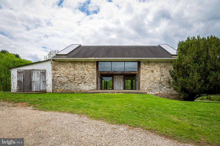 Tucked into ten rolling acres of pastoral Maryland countryside, this property is more than a home—it is a living work of art, a sanctuary shaped by vision, craft, and time. At its heart stands a strikingly modern converted barn, blending glass, stone, and wood in a way that feels both grounded and transcendent.
Walls of glass open the living space to the lush green canopy beyond, while textured stonework rises from the earth like sculpture. This remarkable residence, designed by artisan builder David Naill in collaboration with iconic artist/designers Betty Cooke and Bill Steinmetz, reflects a deep understanding that architecture is both sculpture and shelter—a canvas for light, shadow, and the human experience.
Inside, the barn home is elegantly spare, with open volumes and thoughtful lines that dissolve the boundaries between indoors and out. Each element is intentional. Each surface, eloquent. This is a place where time slows and clarity deepens.
The surrounding barns and outbuildings, filled with history and potential, await their next incarnation—studios, workshops, guest quarters, or gathering spaces. Just beyond the main structure, the property also includes a modest three-bedroom farmhouse, offering additional living space or flexible use for extended stays, caretakers, or creative reinvention.
This is a property rich with possibilities. All structures and systems are being sold as-is and will require thoughtful restoration or enhancement. The listing includes four tax IDs (2305 and 2307 Paper Mill and two on Wetherbee) One of the Wetherbee Tax ID's provides access to the property via the Wetherbee Court cul-de-sac. For those with vision and heart, this is a rare opportunity to carry forward a legacy of design, innovation, and reverence for the land.
Here, in one of the region’s most extraordinary offerings—where the air is sweet, the trees speak softly, and the sky stretches endlessly—you’ll find space not only to live, but to reflect, create, and connect