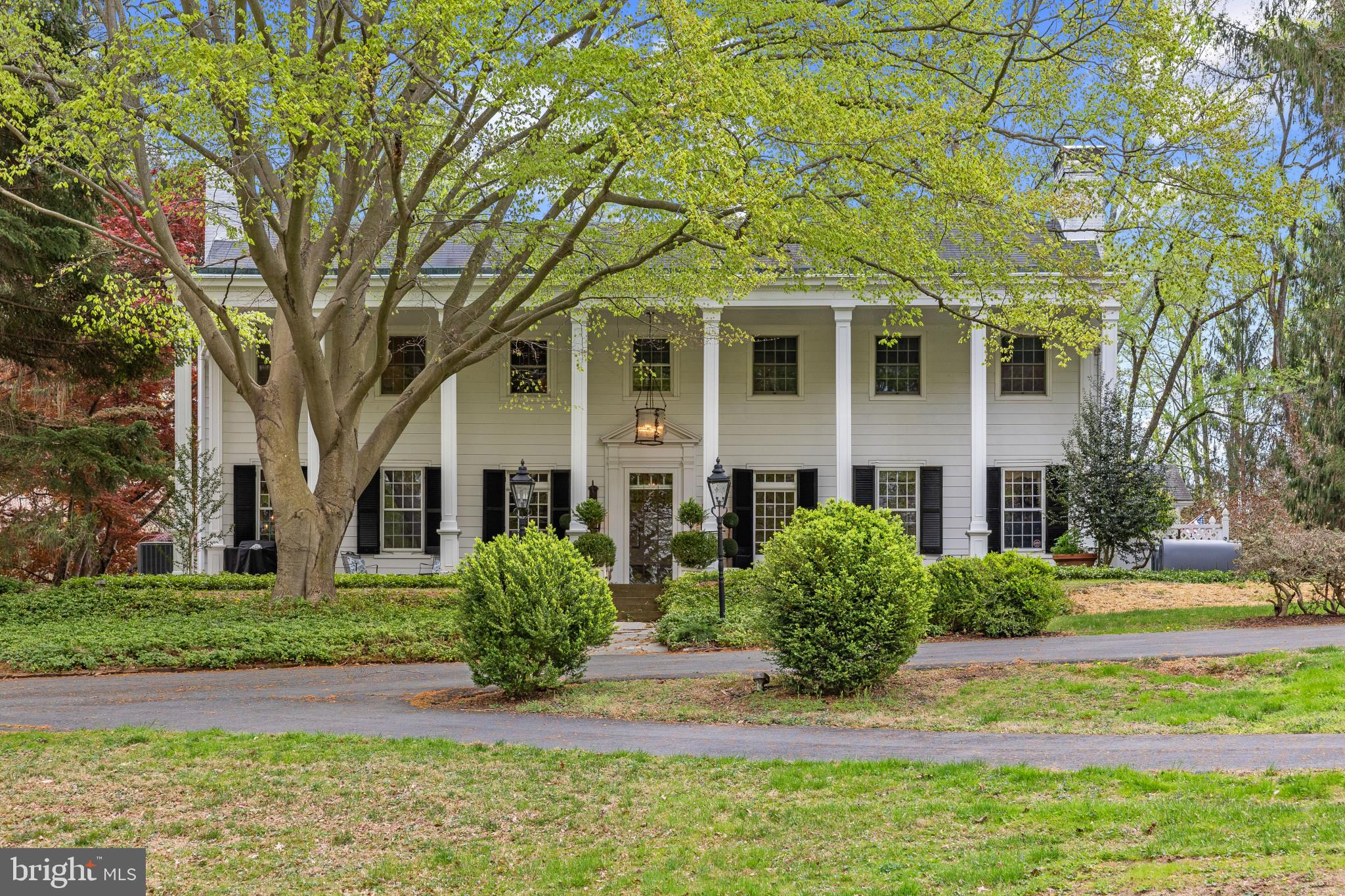 Tucked away on beautifully rolling and wooded grounds, this 1934-built Southern Colonial blends timeless charm with understated elegance. Surrounded by mature specimen trees, this home offers exceptional privacy and serenity. The grounds are remarkable, with expansive lawns, wooded areas, a tennis court, and access to walking trails at Gunpowder State Park. Parking is plentiful with a newly constructed 3 car detached garage with overflow parking and a circular driveway in front of the home.
A classic two-story columned porch opens to a gracious foyer setting the tone for the rest of the home. the main level boasts high ceilings, rich moldings, arched doorways, wide peg hardwood floors, and multiple fireplaces. The grand living room is accented with a fireplace with custom moldings and built ins and large windows with beautiful view. An oversized great room offers impressive scale, ideal for entertaining or movie nights and also has striking views. The charming & tastefully kitchen has and granite countertops as well as new stainless steel appliances. Adjacent to the kitchen is a quaint and light filled breakfast room with access to the side yard and garages. A formal dining room is located just off the kitchen.
At the heart of the main level is a spacious bar room—perfect for entertaining—with extensive cabinetry, countertops, a wet bar sink, and an ice maker. Off the kitchen is a generous mud room, which could easily be transformed into a charming, sun-filled breakfast room.
Two staircases lead to the second level, where a wide central hallway connects four bedrooms and three full bathrooms. The primary suite includes a generous bedroom, beautifully renovated bath, and walk-in closet. A rare opportunity to enjoy classic architecture, privacy, and flexibility in a truly special setting.