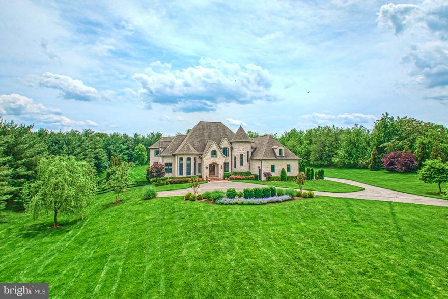 This lavish Creighton Enterprises construction seamlessly blends French Norman-inspired charm with luxurious modern amenity where 3.87 serene Grenata acres lead to the home’s captivating black-tie welcome. Beyond the handsome entry, more than 8,000 square feet are warmly sophisticated with wide-plank floors, bespoke sunlit windows, graceful staircases, and alcoves both intimate and grand. A masterpiece of design and detail, your kitchen invites with ivory tones, intricate molding, and captivating range hood as its professional-grade appliances and expansive countertops foster both beauty and function. Let friends linger with wines selected from the lower-level cellar as you prepare grill-ready bites for parties gathering outside. Here, the oversized stone and brick-lined hardscapes, three cascading waterfalls, firepit, and shallow-edge pool inspire sprawling seasonal fun extending onto the fence-wrapped greenspace. Toss toys for a four legged-friend, or simply savor a poolside-read selected from the home’s most charming space, a tour-worthy wood-clad library. Here, both business inspiration and sorted stories can be reached assisted by the quintessential rolling ladder. Select something joy-filled for playdates in the loft, or sneak away for quiet within any of the nine soothing bedrooms. With seven rooms accommodated by en suite baths, the estate caters to both privacy and comfort. The main-level guest suite offers a haven for long term guests, while the indulgent primary features dual custom closets, oversized spa-like shower, and place for bubbles. While on tour, note the three-floor-access elevator, pair of laundry rooms, showcase-ready five car garage, and a fully finished lower level where you’ll host both game nights at the bar and overnight-stays. Nearby, Historic Leesburg, bustling Village at Leesburg, Wegmans, favorite dining, shops, festivals, and commuter routes await, along with surrounding adventure within greater Hunt and Wine Country.