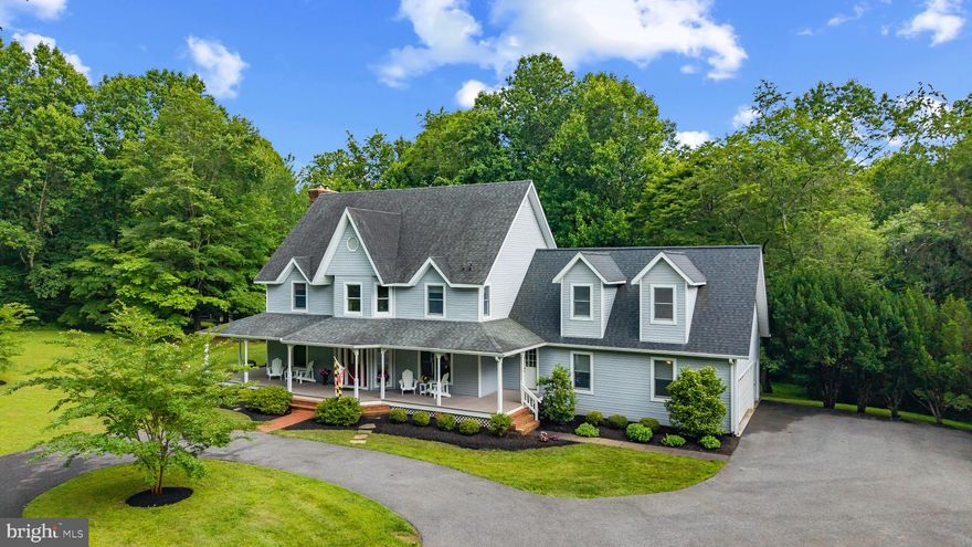 Welcome to this custom Victorian home nestled on 6.4 acres backing to the Triadelphia Reservoir. Located in Howard County’s Kalmia Farms community, the property presents an incredible array of wonderful living spaces both inside and out.
A circular drive approach brings you to the impressive three-level home with an amazing wraparound front porch. The front door opens to a two-story foyer with rich hardwood floors that grace the main level. The living room features a repurposed historic fireplace mantle and two sets of French doors accessing the porch, while the formal dining room is adorned with elegant crown moulding, chair rail moulding, and wainscoting. A large private study contains a wall of handsome cherry wood built-ins for books and storage, and coordinating crown moulding. The kitchen is equipped with cherry wood cabinets, granite counters, a center island with a breakfast bar, recessed and pendant lighting, ceramic stone backsplash, a pantry, a built-in workstation, a built-in bar with a sink, and a breakfast room that leads to the screened porch. The great room boasts soaring cathedral ceilings with exposed beams, an exposed brick wall with a wood burning fireplace, and two sets of French doors to access the screened porch and the brick patio. A convenient mudroom hosts built-ins with an additional sink, an additional refrigerator, a second staircase leading upstairs, and access to the garage, front porch, and back exterior. The owner’s suite presents a walk-in closet and an attached private bathroom with a dual sink vanity, a built-in window seat, and a huge shower with a frameless glass door and built-in bench seat. Upstairs you’ll also find the convenient laundry room, plus three additional bedrooms – one with access to a shared hall bathroom, and one with a private bathroom and large walk-in closet. Downstairs, the lower level provides plenty of additional space for relaxation and entertainment. The rec room has a cozy wood fireplace, custom built-ins, and a built-in wet bar. You’ll also find a billiard room, a bonus room with walk-out access to the lower patio, a half bath, and an unfinished room for storage space. The serene and private property offers plenty of space for outdoor living and entertaining – two patios, a screened porch, wraparound porch, and beautifully-landscaped yard surrounded by trees. This home is situated in a quiet enclave surrounded by woods and within walking distance to a reservoir and trails, convenient to various commuter routes, and central to Baltimore and DC.