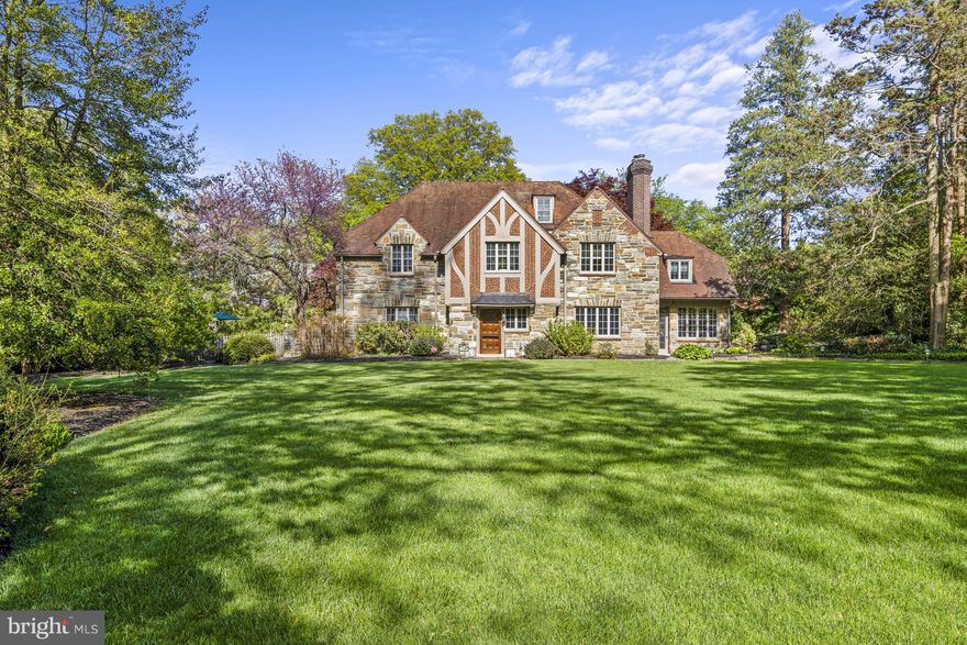 A Westover Hills classic with timeless appeal at the corner of a tree-lined byway, 1001 Westover Road stands as a rare convergence of architectural preservation and modern ease, as Old-World charm meets contemporary life. Designed in 1928 by Philadelphia architects Wallace and Warner, renowned for their European-inspired houses, the residence is a distinguished example of English Tudor Revival style built at the height of American craftsmanship. Its intricate stone-and-brick façade, crowned by a striking red tile roof, sets the tone before you reach the threshold, the first steps on an exceptional journey. A substantial paneled oak door opens beside the original copper-domed lantern, ushering guests into a foyer that is grand and rooted in artistry. The handcrafted Mercer tile floor was created at the Moravian Pottery and Tile Works, emblematic of the Arts & Crafts movement. Brass and wrought-iron balusters and a richly patinated oak handrail grace the staircase. 
Throughout the home, original character is celebrated. A carved mantel anchors the living room, while a library wrapped in lime-washed oak offers an intimate retreat. Sconces and chandeliers exude ambience. Vintage bathroom fixtures and tiles were preserved wherever possible. A south-facing sunroom—currently used as an artist’s studio—glows with natural light, offering an inspiring space for creativity, reading, or quiet retreat. Yet the home is far from a museum piece. Its spaces reflect how people live today. The kitchen is a study in beauty and utility, designed for serious cooking and effortless gathering with professional-style appliances and generous cabinetry, including an original floor-to-ceiling cupboard. The layout is thoughtfully organized, with distinct prep and cooking zones surrounding a large central island. Recent additions have been executed by Dewson Construction. A family room with radiant heat flooring, an expansive mudroom with double closets, and an oversized three-car garage integrate seamlessly with the original structure. Above the garage, unfinished space offers the opportunity for a guest suite, studio, or private office. 
Upstairs, spacious six bedrooms provide flexibility for family and guests. The primary suite is a serene haven with dual closets, including a generous walk-in closet with a dressing area and under-eave storage. A large second-floor laundry room connects to an original cedar closet, blending practicality with period detail. Modern comforts are woven throughout, including abundant storage, energy-efficient, UV-resistant windows and zoned heating and cooling. The home’s flow speaks to contemporary living, with formal and informal rooms connected in a circular layout that makes entertaining feel effortless. Set on a lush 0.66-acre corner lot, the grounds are a private sanctuary of mature trees, curated terraces, and intimate garden moments. A bluestone patio invites al fresco dining, while a tranquil Zen pond offers reflection. Stone pathways illuminated by copper landscape lighting wind through the property, and a fenced yard provides space for play and peace of mind. As this exceptional home approaches its centennial, it offers something increasingly rare: authenticity without compromise.