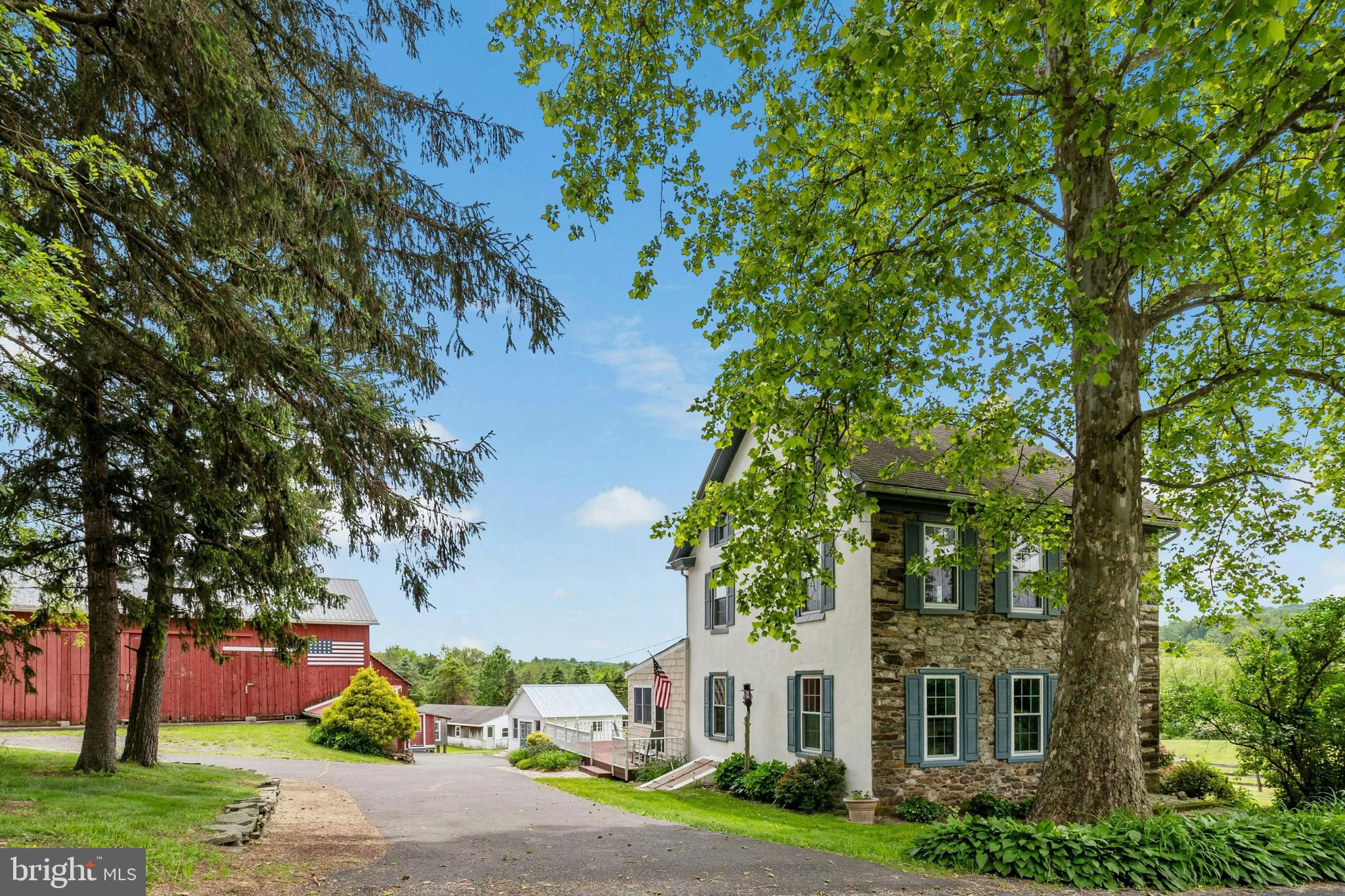 This 12-acre Bucks County farm offers sanctuary in its many delights, from the expanded and updated farmhouse to the large bank barn and multiple outbuildings. Enjoy the peace and tranquility of the rural surroundings, including a large pond and wide fields, in every season.
A stuccoed circa 1800 stone and plaster farmhouse is a haven of warmth and antiquity. The family room, rustic yet cozy with its stone and cedar walls and sliding glass door, makes the hardiest of winter storms seem distant. The eat-in kitchen is a blend of true country flavor and modern convenience. Random width wide plank wood floors, hand-hewn beams and Jotul gas stove complement granite counters, stainless Viking appliances, and soapstone farmhouse sink. Ample living room and dining rooms with an exposed stone wall and beams, hardwood floors, and convenient powder room complete the main level.
Brimming with charm and sought after amenities, the primary suite has wide plank wood floors, a walk-in closet, and renovated ensuite bath with subway tile, clawfoot tub, and converted drysink vanity. Three additional bedrooms, a sitting room, and 2021 full bath will accommodate friends and family.
The farm offers endless opportunities. A circa 1850 bank barn and other outbuildings can house animals, equipment, hobbies, collections, home office and workshop. Bass and bluegill can be found in the pond, perfect for a summer afternoon of fishing. Commuter routes, shopping, dining and entertainment destinations are just a short drive away.