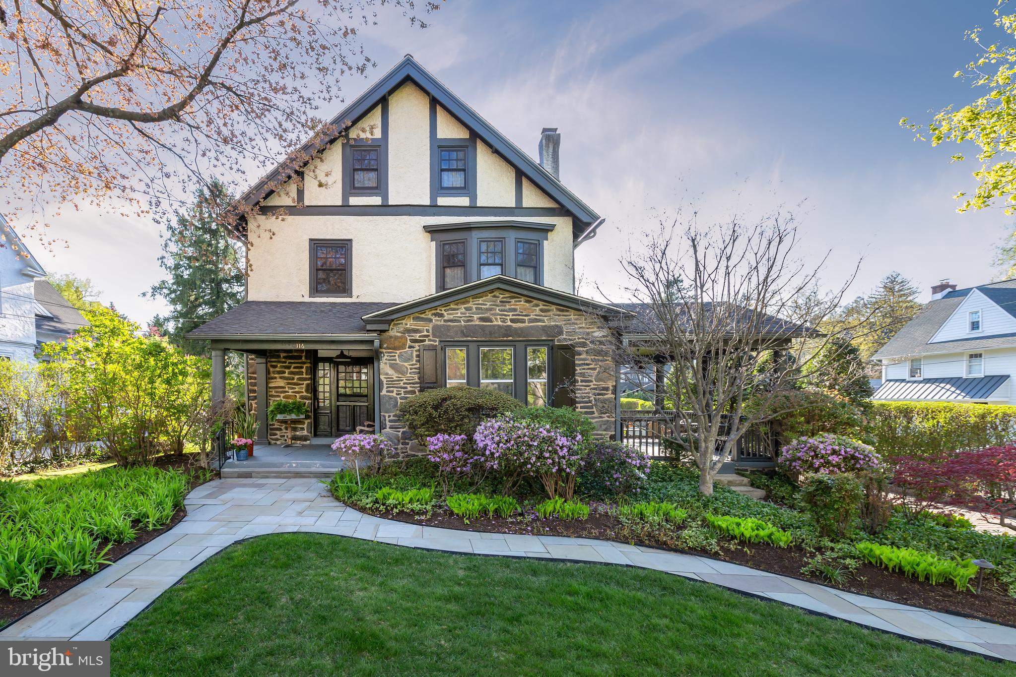Welcome to 116 Llanfair Road, a distinguished stone-and-stucco Colonial set on a private corner lot in one of the Main Line’s most coveted locations. Located on a quiet street just a short stroll from Suburban Square and the best of Ardmore, this residence offers the perfect balance of privacy, walkability, and convenience. Built circa 1911 by renowned local developer Joseph Dyson, the home exudes timeless character with deep-silled windows, original hardwood floors, soaring ceilings, substantial millwork, and exceptional craftsmanship throughout. Thoughtfully updated for modern living, the home features a bright, open floor plan, a fully renovated kitchen and bar area, and an expanded primary suite—ideal for everyday living and effortless entertaining. There’s so much to fall in love with at 116 Llanfair!
A manicured hedge frames the gracious front porch, welcoming you into a warm and elegant interior. The sunlit foyer, accented by sidelights and a transom window, sets a tone of classic sophistication. The living room is both grand and cozy, centered around the original gas- converted fireplace and offering direct access to the charming side porch. The formal dining room—with a stunning bow window—has often served as a flexible extension of the living space, perfect for gatherings large or small. At the heart of the home is the chef’s kitchen, beautifully renovated with custom cabinetry by Village Handcrafted Cabinetry, stainless steel appliances including a Wolf gas range, marble countertops, a stylish tile backsplash, and a built-in bar. A powder room completes the main level.
Upstairs, the grand staircase leads to the serene and spacious primary suite, featuring a luxurious updated spa-style bath. Two additional bedrooms—including one with an en suite—complete the second floor. The third level offers three more generously sized bedrooms and a newly renovated hall bath. In total, the home provides five bedrooms, three and a half baths, plus a bonus office—each space thoughtfully designed and well-appointed. Outside, the large, level lot enhances the home’s stately presence. The backyard is a private oasis with lush landscaping, a rear slate patio, and a fully finished detached studio—ideal as a home office, art space, guest quarters, or a party room for entertaining.
Located in a vibrant yet peaceful neighborhood, the home is just steps from Suburban Square’s shops, restaurants, and year-round farmers market. Families can choose between two award- winning high schools—Lower Merion or Harriton—with Lower Merion High School conveniently nearby. Commuters will love the close proximity to the Ardmore Train Station, offering Regional Rail service to Center City and Amtrak access to New York City. With its rare combination of historic elegance, modern upgrades, and an unbeatable location, 116 Llanfair Road is more than a home—it’s a Main Line lifestyle. Don’t miss your chance to make it yours!