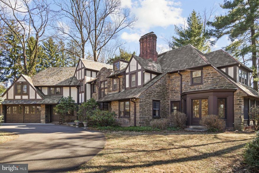 Steeped in rich history and classic architecture, this authentic English Tudor style home (Circa 1926) was designed by renowned Philadelphia architect Charles Rabenold, and was named “The Wilmarjohn” in honor of the original owner’s three children. Later, it became known as the “House of a Thousand Lights” because of its stunning holiday light display. The striking exterior features grand stonework,  half-timbering, a hipped slate roof with copper gutters and downspouts, embodying timeless craftsmanship and elegance.  Originally on 17 acres, today the 6 Bedroom, 3.1 bath grand home is situated on1.23 acres along a quiet neighborhood street. A circular driveway, framed by mature shade trees, vibrant rhododendrons, and sweeping lawns, creates a picturesque approach. The grounds offer ample space for croquet, hide- and-seek, or quiet afternoons by the inground pool. Inside, the extraordinary home transports you to another era.  Plaster over lathe walls, generous millwork, deep baseboards, wainscoting,  tall ceiling height, and quarter sawn & hardwood floors grace the residence. Two staircases, two wood fireplaces,  and grand scale add to its distinguished character.  The expansive living room, featuring a brick fireplace, opens to the outdoors through French doors to a charming flagstone terrace. It is flanked by a banquet sized dining room with a china cupboard and bay alcove, and an inviting sunroom adorned with handmade “brick” tiles in a basketweave pattern  and Mercer tile accents. The sunroom, with French door bays at either end, seamlessly connects with the outdoors.  A cozy library/home office, with wood fireplace, offers a serene retreat. A beautifully updated cook’s kitchen blends modern convenience with vintage charm. Handsome wood cabinetry compliments original pantry cabinetry with glass uppers, pull-out cutting boards and vintage hardware.  The kitchen boasts stainless appliances, including a 5-burner Thermador gas cooktop,  travertine backsplash and charming “Love Bird” Mercer tile accent.  Granite counters and a center island allow for a breakfast bar for casual dining, while a convenient Butler’s pantry/laundry are a segue to the sophisticated dining room. The 2nd floor includes all 6 bedrooms, each with hardwood flooring and ample closets.  The en-suite primary bedroom offers expansion potential through a “false” wall, which could serve as a dressing room, new main bath, nursery, or home office.  The additional bedrooms share two hallway baths. A spacious part- finished walk-in attic with pull-down stairs adds floored storage, while a bonus room with glass French doors opens to a balcony, overlooking the inviting front foyer. On the 3rd floor, a large finished room provides ideal space for a playroom, gym, or media room.  This quality-built home has a foundation constructed of full thickness stone walls, and features a bulkhead and Bilco doors for egress, and plumbing if a bath is needed.  Outdoor highlights include an oversized 2-car carriage garage, and updated concrete pool (10’ deep) with a  safety gate and pool shed. Utilities are public sewer, water, natural gas, and steam radiator heat. Very well maintained, but ready for some updating, this remarkable home has offered decades of cherished memories for family and friends. Close to shopping, public and private schools, and major roads, this historic home blends timeless elegance with modern living -truly a once-in-a-lifetime opportunity!