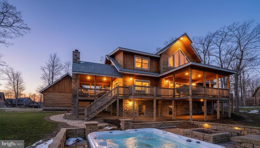 This striking 5 bed/7 bath log home sits in one of Wisp Mountain’s most sought-after locations, offering a warm four-season retreat just minutes from Deep Creek Lake, Lodestone Golf Course, Wisp Resort, and the area’s top dining and recreation. Seasonal lake views from the living room and deck enhance the setting and connect the home to its surroundings. The main level features a bright, open layout with a wall of windows, a floor-to-ceiling stone fireplace, and a well-equipped kitchen with granite, stainless appliances, gas range, farm sink, and a large island. Sliding doors extend the space onto an expansive deck with a covered outdoor fireplace, making indoor-outdoor entertaining effortless. A main-level primary suite with deck access and a spa-style shower anchors the first floor, while the upper loft with wet bar and two additional suites provide comfortable accommodations. The lower level adds a full family-fun zone with a pool table, arcade game, wood-burning fireplace, wet bar, another primary suite, and a bunk room. Outside, a large stone patio with built-in firepit seating and a private hot tub complete the package, offering multiple places to gather, unwind, and enjoy the mountain setting. A detached two-car garage with space above provides excellent storage for vehicles and gear. The property is also equipped with a whole-house Generac generator, ensuring dependable backup power in every season. Blending craftsmanship, comfort, and a prime location close to everything Deep Creek offers, this home stands out as an ideal full-time residence, vacation property, or rental investment.