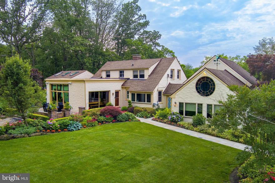 Discover your private haven at 922 Merion Square Road, an enchanting expanded Contemporary Cape nestled on a full acre in the heart of Gladwyne. Just a short stroll to the village center, playground, tennis courts, restaurants, markets and transportation, this beautifully maintained home offers a rare blend of classic charm and modern comfort, wrapped in a setting of quiet beauty and mature gardens.
Inside, the home opens with a gracious sense of light and warmth. A formal living room with a wood-burning fireplace sets the tone, while just beyond, the open kitchen provides a comfortable and well-equipped workspace with granite countertops, custom wood cabinetry, and ample storage. Opening directly to the brick-floored dining room, where floor-to-ceiling windows frame serene views of the private grounds — a space that captures the spirit of the home with its blend of natural materials, garden views, and timeless appeal.
Steps away the home unfolds into a stunning great room with soaring ceilings, richly stained wood details, and an entire wall of custom built-in shelving. Flooded with southern light and anchored by its sense of scale, this room is equally suited for large gatherings or quiet evenings by the fire.
The first-floor primary suite is tucked just off the living spaces and offers a true sense of retreat. High volume ceilings and abundant natural light define the space, while an updated bath with soaking tub, glass-enclosed shower, and a spacious walk-in closet enhance both luxury and function. Flanking the entrance to the suite are two custom bookshelves that conceal a laundry area on one side and a temperature-controlled wine cellar on the other, complete with a handsome live-edge countertop and bespoke display storage.
Also on the main level are a second bedroom, an additional full bath and interior access to a two-car garage. Upstairs are two more comfortable bedrooms and a neutral hall bath. Above the garage and accessed from a separate staircase, a generous bonus space offers great flexibility — ideal as a playroom, gym, studio or as currently purposed as a quiet home office.
Throughout the home, gleaming hardwood floors, central air conditioning, and nearly all new windows offer peace of mind and everyday ease. A full-house generator and an unfinished basement with plentiful storage and a second washer and dryer add further practicality.
Outside, the property unfolds into a lush, secluded garden setting. Stone paths, shade trees, and carefully tended plantings create a peaceful outdoor world — perfect for alfresco dining, weekend gardening, or simply enjoying the sounds of nature in your own private corner of Gladwyne.
922 Merion Square Road is a rare opportunity to enjoy both seclusion and walkability, history and thoughtful renovation — a home that offers ease, character, and room to live beautifully.  
________________________________________