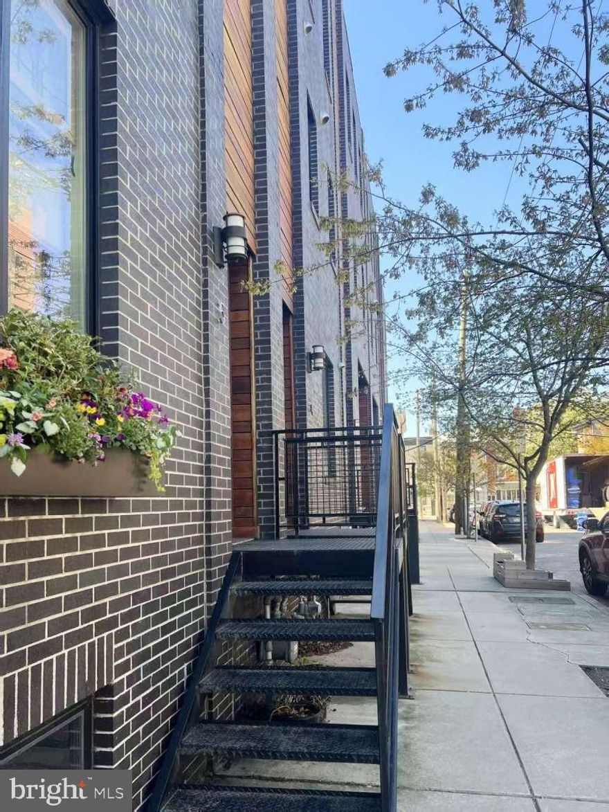 Welcome to Moyer Court! This beautiful modern townhome is perfectly situated in the heart of Fishtown, within walking distance to some of Philadelphia’s most popular restaurants, breweries, distilleries, and coffee shops. Convenient access to the Market Street line, Center City, major highways, and surrounding suburbs makes commuting a breeze. This 25-foot-wide end-unit home, set within a shared courtyard, offers a unique combination of space and flexibility. As you arrive, you’ll appreciate the oversized private one-car garage, complete with pro-slat wall system and an EV charging outlet. Inside, the home features 10-foot ceilings and a long entry hallway that leads to a rear bedroom. Just off this room is a small backyard—perfect for a quiet and private outdoor retreat. The bedroom also includes a full bathroom with a tub. The second floor opens up to a bright and spacious main living area, highlighted by a full wall of built-in bookshelves. The modern kitchen features a large walk-in pantry, along with a convenient half bath. Glass accents showcase a striking floating staircase, allowing natural light to flow through the upper levels. The open-concept layout is ideal for both everyday living and entertaining. On the third floor, you’ll find two generously sized bedrooms, each with walk-in closets featuring custom shelving and storage. The primary bathroom offers a double vanity, a custom-tiled shower, and a large lux air-jet soaking tub for a spa-like experience. Continuing upward, a wet bar area sits at the base of the next staircase, leading to the rooftop deck—perfect for entertaining or relaxing. The roof deck features a combination of green roofing and wood decking, with ample seating space and room for a dining table for six. Enjoy sunsets, fireworks, and sweeping, unobstructed views of the Philadelphia skyline. The partially finished basement provides laundry, plenty space of storage and a home gym. The unit is also walking distance from multiple parks and steps from Adaire, Fishtown Rec, and Swimmo.