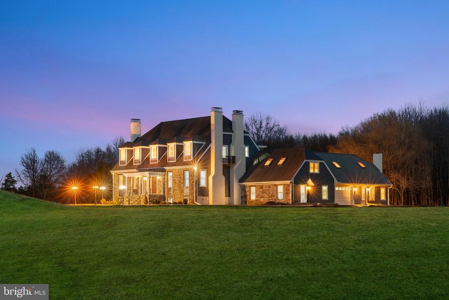 Tucked near the winding beauty of the Delaware River, hidden from the hurried pace of the world, lies a 22-acre estate—a rare and timeless sanctuary in the heart of Bucks County. For those fortunate enough to follow the graceful white gravel path that winds through open fields and under ancient trees, a storybook setting slowly unfolds.
The main house rises in quiet splendor, its exterior a harmonious blend of stone, cedar, and slate—a testament to old-world craftsmanship and enduring design. The first glimpse is like stepping into a different era, where refinement isn't shouted but whispered through every thoughtful detail. Doric columns frame the entrance, guiding guests into a porcelain-paved foyer bathed in light from a crystal chandelier. Above, a grand staircase spirals upward, hinting at the treasures waiting beyond.
To the right, a handsome library beckons, warmed by a carved wooden fireplace mantel. Opposite, a large parlor opens into view, its herringbone  exotic hardwood floors and antique French-style fireplace offering a quiet place to pause and admire the past. A formal dining room, anchored by a carved marble fireplace and a magnificent bay window that captures the golden afternoon light.
Beyond the dining room lies a kitchen straight from an American dream. Marble, European tiles, and custom Modern cabinetry speak of both elegance and function, while a wood-paneled ceiling adds warmth and character. It opens into a large den where antique barn beams stretch overhead and a bespoke carved fireplace glows softly. Here, an informal dining area  offers the perfect place to gather, its beveled glass French doors leading to a wide stone patio that spills into the open fields beyond.
Tucked discreetly off the den is a well-appointed laundry area, complete with its own bathroom, shower room, and access to the garage. But this house holds secrets. Behind a hinged bookcase lies a passage that leads to the in-law suite—a private haven above the garage, complete with its own fireplace and a separate entrance for added privacy.
Upstairs, the main house offers three spacious bedrooms and two full baths, each brimming with light and quiet elegance. The master suite is a retreat unto itself, with a gas fireplace framed in carved marble, a small balcony for morning coffee, and a luxury bathroom.
Outside, just a few hundred feet along the path, a charming guest cottage waits, its own deck and expansive paved parking area perfect for hosting visitors. Next door, a classic barn opens to a fenced pasture, ready for horses, hobbies, or simply daydreams of countryside life.
Though the estate was completed in 1992, and completely renovated in 2025. it has been lovingly maintained and thoughtfully updated recently. Modern systems, an automatic backup generator, a full-sized basement, and a fully floored, insulated attic ensure comfort without compromise.
A rare opportunity to own one of Bucks County’s most unique and refined estates. A Hidden Jewel Along the Delaware offers timeless craftsmanship, modern updates, and exceptional amenities—perfect for luxurious everyday living or stylish entertaining. But more than any feature or finish, what sets this estate apart is its soul. There’s a sense of timeless charm in every room, every view, every breeze that dances through the tall grass. It’s not just a home. It’s a place where stories are made and where life, in all its beauty and richness, can unfold.

Showings start at the Open House on 04/04/2026. Don’t miss your chance to see this beautiful home in person!

Stay tuned for more details and mark your calendar!