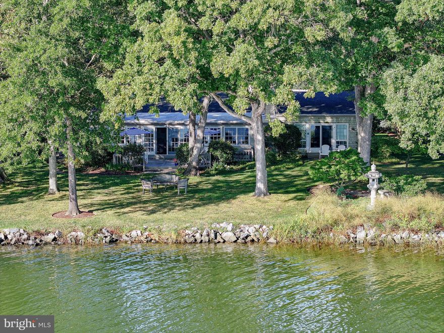 Welcome to your private waterfront retreat just minutes from the charming, historic town of St. Michaels, Maryland. Tucked away on a quiet cul-de-sac in the serene Oakwood Park community along San Domingo Creek, this one-story residence offers four bedrooms, three and a half baths, and a harmonious blend of space and comfort. With approximately 2,839 finished square feet, all on the main level, the home is designed for convenience and ease of living. Inside, generous rooms are enhanced by rich custom yellow pine floors, premium carpeting, and tile. At the heart of the home, the living room impresses with a vaulted ceiling, exposed beams, custom built-ins, and a rustic wood-burning fireplace. A waterfront family room flows into the dining area, while the country kitchen features handsome cabinetry, premium countertops, modern appliances, and a pantry with washer and dryer. The waterside primary suite offers a fireplace, walk-in closet, and a spacious bathroom with dual vanities. On the opposite side of the home, a second bedroom includes an ensuite bath and walk-in closet, complemented by two additional bedrooms with ample closet space (one used as den) and a full bath.  
The exterior showcases cedar shake siding, a welcoming covered front porch, a private patio between the main bedrooms, a large rear waterside deck, a two-car detached garage, and a wide gravel driveway with ample guest parking. The property is served by a private well and septic system, with public sewer hookup approved and coming soon, offering flexibility for future expansion or renovation. This home is part of a unique five-property HOA (fees $600/year) with each property owning 20% of a central community lot, a deepwater dock with five slips, and a historic pavilion available for member events and leisure. Residents also enjoy a kayak rack and a small sandy beach for launching boats or paddle boards. The setting provides not only a comfortable home but a lifestyle of Chesapeake Bay waterfront living.  According to research, the grounds of the five lots and the “Oakwood Association” belonged long ago to the Oakwood Inn, a prominent retreat in the early 20th century. Known for its scenic harbor views and role in local leisure culture, the inn appeared in postcards from the 1930s and was a hub for skating, swimming, pleasure boating, regattas, and log canoe races. Its legacy adds a rich historical dimension to the property, connecting today’s residents to St. Michaels’ vibrant past as a sailing and leisure destination.  There are photos of two pieces of memorabilia at the end of the photo section of this listing for your enjoyment.  See attached documents for HOA information ($600/year per property), easement information, C&Rs, Contract Disclosures, etc.  Flood Zone X, no flood insurance required.  Three-bedroom septic, public sewer hookup available near future.