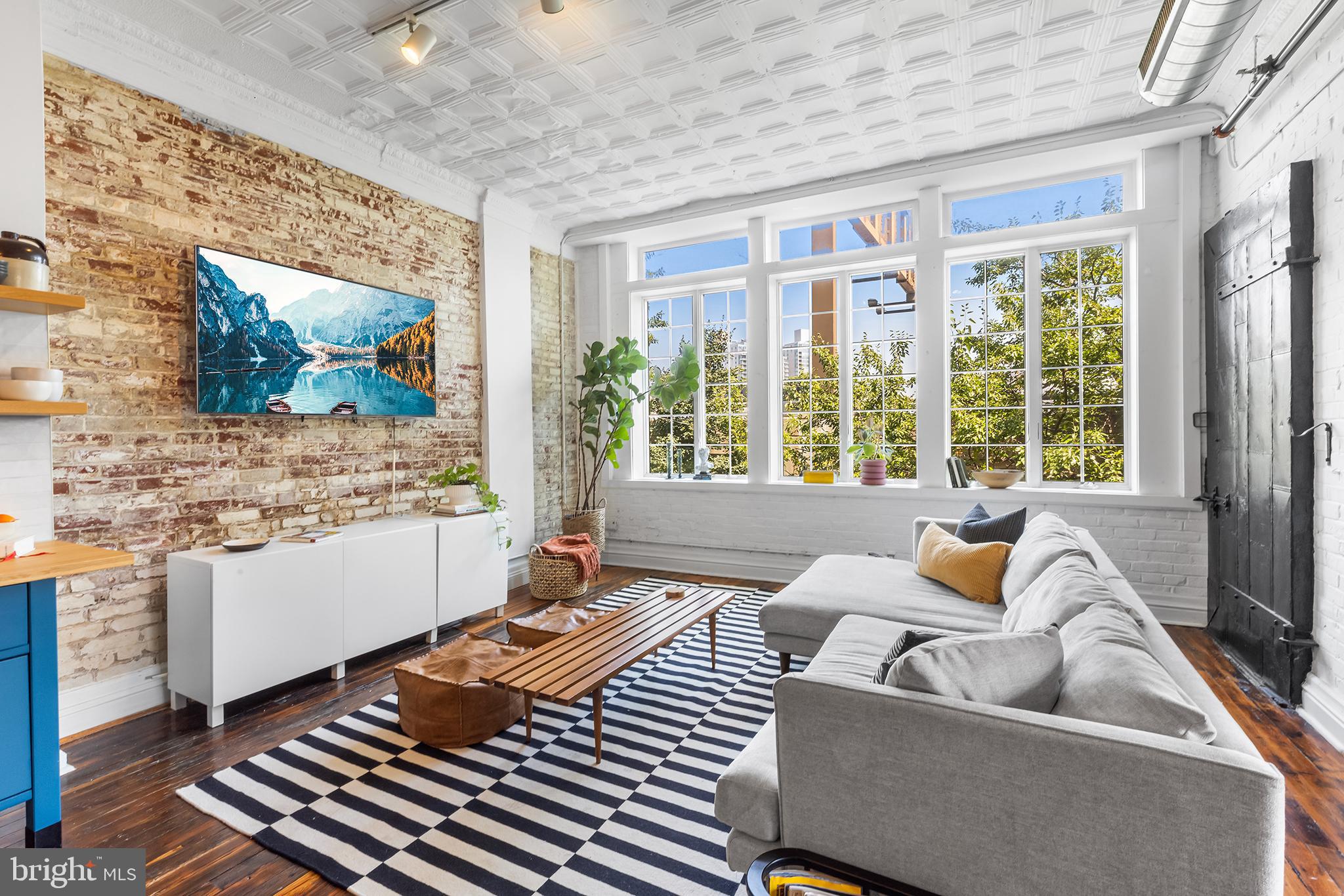 This design-forward 2 bed, 2 bath loft in Northern Liberties blends rich history with thoughtfully curated updates in a former cast iron factory. Located on the second floor of the 1902 building, this boutique condo has five residential units above a street-level storefront hosting a chiropractic office. Up inside the loft you'll find soaring ceilings, exposed brick, large, east-facing windows flooding the open living space, and beautiful hardwood floors. The open living area is anchored by a renovated kitchen - where moody blue cabinetry, butcher block counters, open shelving, brass fixtures, and handmade tile strike the perfect balance between modern function and charm. A cozy dining nook sits beside an old freight elevator door; one of the architectural gems of this unit. The large living space makes for a magical place to sit in the morning - an exceptional amount of natural light streams through the windows - and a delightful place for entertaining in the evening - as this area spills out onto the private, covered porch. One of the standout features of this condo is the truly special patio. Surrounded by red brick and greenery, and finished with painted checkerboard floors, it feels like a European balcony - perfect for morning coffee, evening wine, or a plant-filled sanctuary. Back inside you'll find two bedrooms. The larger is a perfect sleeping space with a sizable closet and south-facing window, and the second bedroom works as a great office, guest room, or nursery. The primary bathroom is a design lover’s dream - a spa-like wet room wrapped in sage green tile, creating a calming atmosphere around a freestanding soaking tub. This bathroom is spacious and has a double vanity. The second full bathroom features a clean, modern stall shower. Tucked beside the entryway door is the in-unit laundry, mechanicals, and a large coat closet. This loft has so much comfort and convenience, with low HOA fees and bike/storage on lower levels. There is also a rare (!!) opportunity: this is one of the few condo associations that allows AIRBNB/short-term rentals (with proper licensing), offering flexibility for part-time residents or frequent travelers. Inquire for more information about purchasing this loft fully furnished. Just steps from Standard Tap, North Bowl, Pietramala, The Kettle Black, and Liberty Lands Park; you can do everything in this neighborhood, while being just a walk, bus, or subway away from the rest of Philadelphia!
