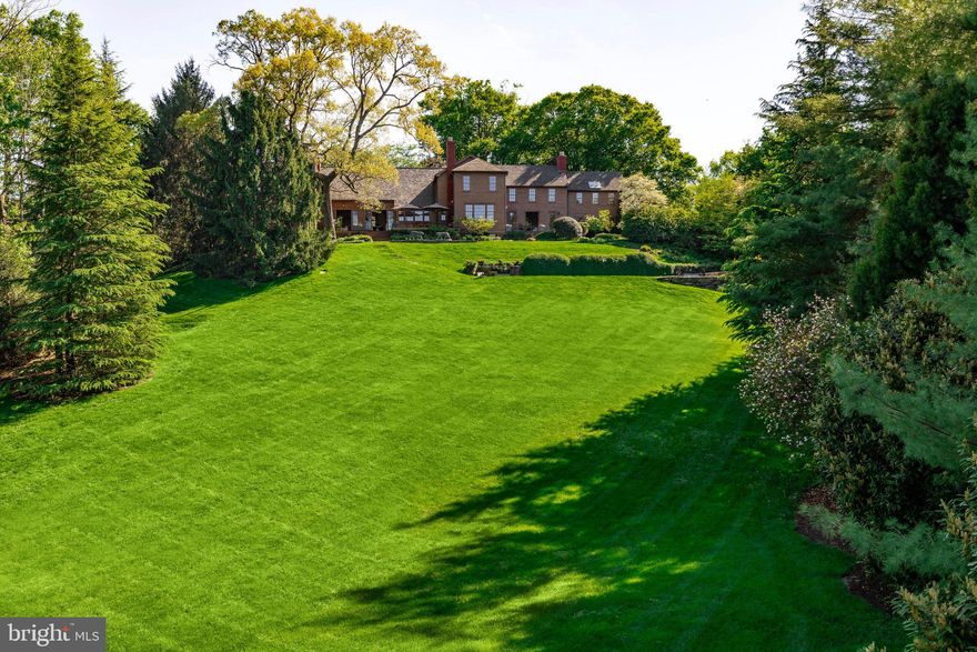 Uniquely nestled on 2.47 manicured, parklike acres in the heart of the prestigious Langley Oaks neighborhood, 6400 Georgetown Pike is an estate of rare distinction. A pair of motorized gates offers discreet entry to the grounds, where a winding pebble driveway orchestrates a graceful approach to the main residence. Originally constructed prior to the Civil War, the home is clad in historic wooden clapboard and evokes the ambiance of a grand mountain lodge, a feeling heightened by the surrounding rolling hills and towering pines, yet juxtaposed by its remarkably central and accessible setting.
 
Inside, a central foyer bisects the main level, artfully dividing formal and informal living areas. The interiors are a masterful fusion of bold historic detail and stylish modernity, recently reimagined in collaboration with renowned designer Thomas Pheasant. Gleaming, dark-stained hardwood floors flow seamlessly throughout. The formal living room is generously scaled for elegant entertaining, opening through triple sets of doors to a flagstone patio. An exquisite fireplace with hand-carved wooden mantle anchors the far wall, while a step down reveals the dignified library, encased in built-ins and aglow with soft architectural lighting.
 
Opposite, the informal wing inspires awe with its soaring 30-foot vaulted ceiling, fully exposing original wooden beams and columns. At its heart lies the chef’s kitchen, complete with a custom wooden prep island and a comprehensive suite of Sub-Zero and Wolf appliances. A large, tiered island bridges the transition into the family room, where a roaring wood-burning fireplace with substantial stone surround commands attention. French doors open to the rear deck, while a wall of windows frames the front lawn.
 
Upstairs, the primary suite occupies its own private wing; a sanctuary of serenity and scale. A vestibule opens to the main sleeping quarters beneath a vaulted shiplap ceiling. The adjoining dressing room impresses with its own vaulted ceiling, extensive built-ins, and rolling library ladder. The luxurious primary bath features dark floor tiles mirroring the dual vanities, which flank a handmade French soaking tub by Naudie. A skylit walk-in shower and separate water closet complete the suite. Three additional bedrooms each with stylish ensuite baths are also located on the upper level.
 
The lower level offers a large recreation room, bonus space with wet bar, dedicated laundry area, and a professional-grade home office. A detached guest house stands adjacent to the main residence, doubling as an oversized garage. The upper level is a private suite, ideal for a home office or fitness studio. Below, a fully self-sufficient residence includes a premium kitchen with JennAir and Sub-Zero appliances, guest bedroom, and full bath.
 
State-of-the-art systems span the estate: Lutron lighting, an advanced LG security system with video surveillance, Geothermal HVAC, central vacuum, and a whole-house generator ensure seamless comfort. The guest house enjoys independent HVAC and security systems.
 
Outdoors, the estate's whimsical grounds blend tiered gardens, mature trees, and extensive hardscaping into a tranquil, curated landscape. Landscape lighting and full irrigation ensure beauty day and night. A large lap pool with automatic cover and adjacent spa enjoy verdant views of the surrounding acreage.
 
Located within the Beltway and just moments from acclaimed Langley High School, the estate is mere minutes from McLean’s town center and the George Washington Parkway into DC. Completely irreplaceable, 6400 Georgetown Pike stands as the apex of luxury country living in one of the Capital Region’s most coveted enclaves.