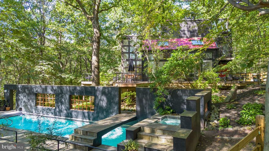 Breathtaking architecture on three wooded acres provides a residence as equally well-suited for entertaining as it is for tranquil everyday living in this Bucks County treasure. The Scandinavian influence is evident in the full walls of glass and dramatic windows that bring the outside in, a central chimney that provides a fireplace on every floor, and the use of natural materials including slate and oak floors. Lovely custom details with a touch of whimsy grace the interior, and the current owners have made extensive improvements. The main floor offers a spacious foyer entrance, library with skylight, powder room and sitting room all on one side of a double fireplace with newly installed woodstove insert. On the other side is the showstopping open living and dining space with vaulted ceilings, floor-to-ceiling windows, custom conversation pit with integrated storage that seats a crowd, and a just-installed wall of custom 12-foot glass bifold doors that allow the separation between the inside and the expansive Ipe wood deck with multiple entertaining areas to all but disappear. The corner breakfast room has two walls of floor-to-double-story-ceiling windows, from which the current owners eliminated a wall and added a breakfast bar to make it more open to the kitchen, where the Scandinavian design principles really come to life. Functional details like a prep sink, pot filler and wine fridge are integrated into the understated warmth and luxury of oak flat-front cabinets alongside fresh quartz countertops and glazed ceramic tile backsplash. The second story has a large central sitting room with fireplace overlooking the living room with a newly renovated terrazzo tile bathroom, two bedrooms, and an office with French doors to a balcony. The third floor is the peaceful primary suite, with a fireplace and sliders to a balcony that spans the entire side of the house and overlooks the wooded hillside and pool area. Soak among the treetops in the gorgeously remodeled en suite, where the tub sits beneath a span of oversized sloped windows, or enjoy the same view from the curbless shower with fluted marble surround. The delightful walkout lower level has a wet bar, large den with oversized French doors to a cobblestone patio, a guest suite with a newly renovated bathroom, and access to the laundry room. Just as stunning as the home itself is the newly plastered pool and spa with flagstone pavers, which are framed by a decorative wall on one side and an expanse of woods on the other. Other exterior upgrades include new elegant black Hardie Batten board siding and a fence encompassing a large area of the yard and pool. In a bucolic Bucks County setting and down a private road, the home is away-from-it-all yet a short drive to Doylestown, New Hope and Lambertsville, making it both a desirable year-round residence and an attractive getaway for Philadelphians and New Yorkers alike.