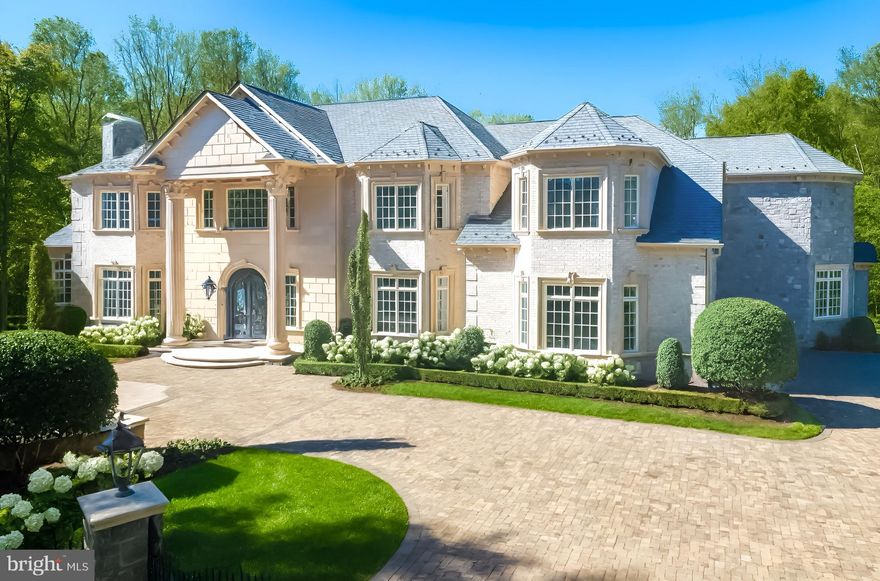 Set along a peaceful, tree-lined lane, 1174 Old Tolson Mill Road reveals a stunning, stone and brick gated estate, with award-winning landscaping by Charles Owen. This gorgeous home with over 15,000 square feet of living space designed by Arlene Christos reflects unmatched craftsmanship and elegant detailing. Offering both privacy and convenience, the property is ideally located just minutes from Great Falls National Park, Scott’s Run Nature Preserve, and the world-class shopping and dining of Tysons Corner. There is a 2-story portico with columns, a custom wood-and-glass door adorned with wrought-iron inlays welcomes you to a two story marble foyer, featuring a grand split staircase beneath a soaring mezzanine inspired by New York’s Four Seasons Hotel. The main level showcases elegant formal living and dining rooms, perfect for entertaining. The great room soars with a 24-foot ceiling and features a striking fireplace as its centerpiece. The gourmet kitchen is a chef’s dream, complete with dual center islands, custom cabinetry, and top-of-the-line appliances, including an espresso machine, warming drawer, refrigerator drawer, and wine cooler. The adjacent family room offers a cozy fireplace, a Meridian surround sound system, and direct access to the terrace, seamlessly blending indoor and outdoor living. Also on the main level, a paneled library features custom built-in shelving and a charming bay window. The guest suite offers a walk-in closet and a spa-inspired bathroom, providing both comfort and elegance. The upper level is host to the primary suite that spans more than 38 feet and feels like a five-star retreat. Its double-tray ceiling, Phantom screened balcony, outdoor hot tub, and travertine-clad spa bath create a sanctuary of comfort and style. Three additional ensuite bedrooms, each with walk-in closets, plus a large laundry room with dual washer/dryer sets complete this level. The lower level is a recreation haven that includes a spacious recreation room with a masonry fireplace, a central wet bar framed by twin wine cellars, a game room, state-of-the-art home theater, and a spa with steam shower and sauna and a generous guest suite.  The home is equipped with 18 interior and exterior cameras, hardwired doors and windows, and a 21-day recording system. Cell signal is enhanced on every level, with integrated smart home automation and a comprehensive security network. A Crestron smart system controls lighting and audio throughout the home.  Security, and motorized shades in Owner's Suite are easily managed from your smartphone. Outside, the estate spans two private acres with fully fenced grounds, highlighted by expansive terraces and meandering pathways. Built for both convenience and performance, the home features a three-level private elevator, dual garage lifts for five vehicles, four HVAC systems, a central vacuum, and an 80kW Generac generator ensuring uninterrupted comfort. Pool & terrace are proposed renderings.