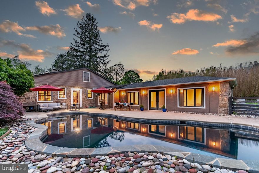 Down a long driveway in scenic Solebury, this extraordinary property slowly reveals 3.4 gently rolling acres with Aquetong Creek meandering along its wooded edge, a home where architecture and landscape converge with ease. The centerpiece is the main house, built from an original stone horse barn. A dramatic great room welcomes with vaulted ceilings and three skylights that usher in shifting daylight. A modern, glass-fronted wood stove set on an elevated mantle framed by stone and hewn from original barn wood, with bamboo floors bringing warmth and flow through the public spaces. The open dining area, kitchen, and breakfast nook are united by thoughtful finishes and organic materials, with amazing views of the pool and gorgeous woods beyond. In the kitchen, Bucks County soapstone tops the island and cabinetry. A Shaw farmhouse sink sits beneath a sunny window, while a coffee bar is smartly tucked into a pantry nook, keeping the essentials close but the counters clear. A second pantry near the laundry, with a folding station and work sink, adds function and storage. The main primary bedroom suite is layered in luxury. Italian tile floor with radiant heat runs throughout a space that includes a private sitting and dressing room with a sleek BoConcept wardrobe, an en suite bath with a walk-in shower offering both rain and handheld options, a spacious walk-in closet, and a bedroom that opens to the sculptural, free-form swimming pool just steps away. The construction is modern and sleek with original stone framed as accent on two walls. Two additional bedrooms share a modern, skylit bath with clean lines and curated finishes. Upstairs, a loft space offers flexibility for a number of uses. Beyond the main house, a separate one-bedroom in-law suite with its own private entrance and outdoor area offers myriad possibilities as dwelling or expanded home office. In-law suite includes full recently remodeled kitchen, private laundry, dining area, and relaxing living room with glass-front wood stove. Throughout, the vibe is relaxed and bright. A handcrafted Amish-built garage holds four vehicles and features an unfinished upper level with electricity already in place for easy use as studio, office, yoga loft, or music room, with gorgeous views of the stream and woods. A large Generac generator powers the entire main house (including pool, laundry, and heat/AC). The gorgeous, private pool sits in full sun, with dark-plaster black-bottom construction that keeps the water warm naturally and creates a stunning effect when lit at night. Natural stone steps lead down to secondary patio and firepit.