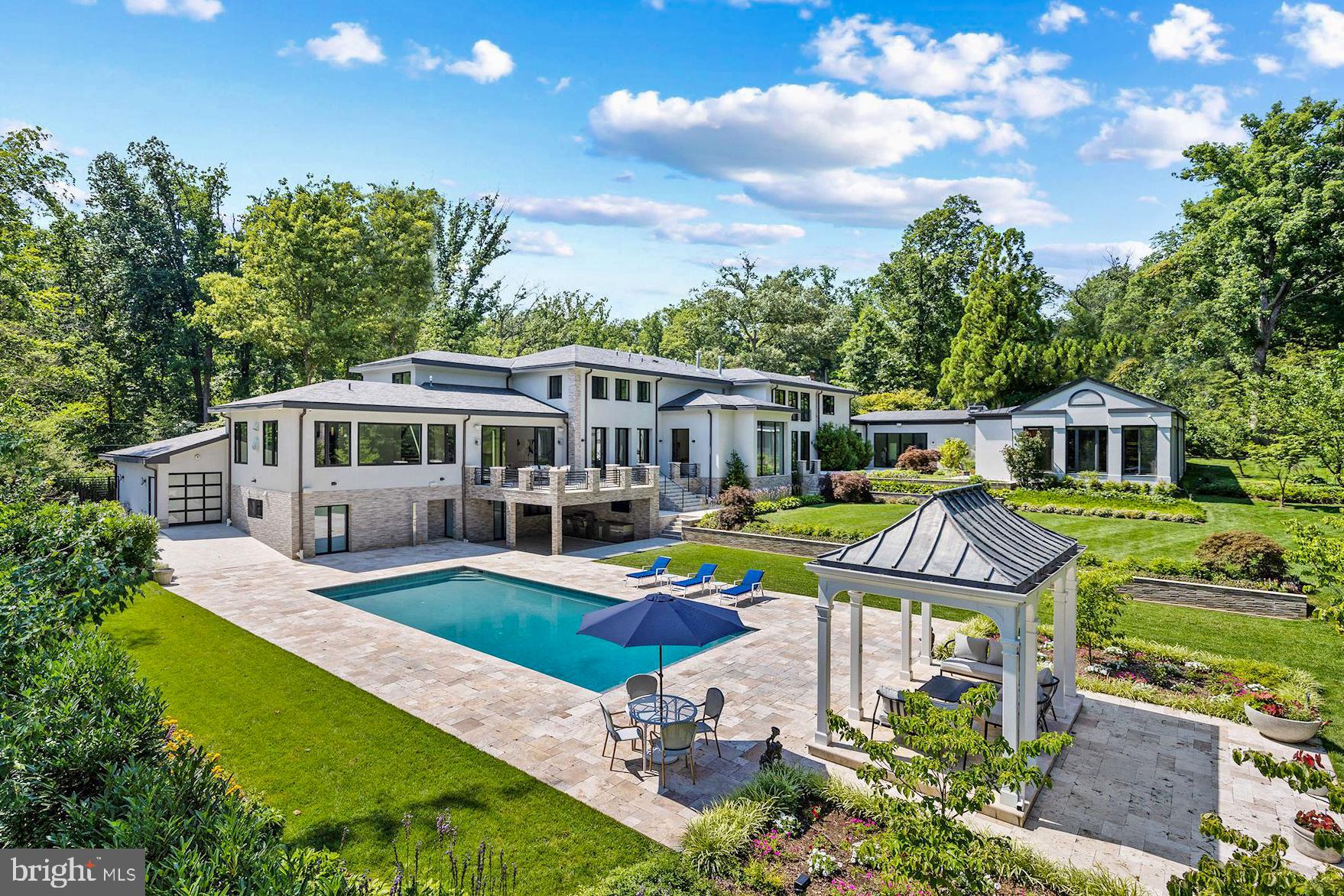 Prominently positioned yet discreetly tucked away on a quiet, winding section of famed Fernwood Road in legendary Bradley Hills Grove, this is one of those truly special homes where not a single detail has been overlooked. Painstakingly reinvented with obsessive attention to detail and the finest international materials, all 15,000 square feet of living space has undergone a complete transformation — the result of which is an estate with an old soul clad in contemporary finishes. The driveway, with its intricately inlaid criss-crosses of grass, evokes a distinctly Californian charm conveying a sense of airiness carried throughout the home. Light floods the 19 foot greeting hall and gives way to a stunning open-slab glass staircase whose transparency allows light from the double-height wall of windows beyond to permeate inwards. Fine workmanship and top-notch materials are evident everywhere, an example of which can be seen with custom built imported interior doors. Elegantly proportioned formal spaces live up to the substantial square footage, enabling entertaining on the grandest of scales. Yet, the thoughtfully designed floor plan is equally apt at accommodating everyday living. As the heart of the informal space, the chef’s kitchen boasts an oversized quartz-topped center island and two large windows letting in abundant natural light. Sleek European style cabinetry conceals a full suite of top-of-the-line Miele appliances, including a 48-inch commercial range and twin wall ovens. A large primary suite completes the main level, facilitating multigenerational living. Reaching the upper level via stairs or one of two elevators, the second primary suite, with its raised ceiling, has three sets of French doors which reveal sweeping views of the rear garden and pool. Its spa-inspired bath features twin floating vanities, a freestanding tub, a walk-in shower concealed by custom smoked-glass doors, and, along with every other bathroom in the home, radiant heated floors. The custom dressing room is equally minimalist with dark mirrored doors concealing all shelving and a large center island. Amenity-rich, the estate boasts a fully-equipped covered outdoor kitchen with Wolf appliances, as well as an extensive stone terrace. The terrace steps down to an immaculate patio housing the newly resurfaced outdoor pool with automatic retracting cover and a charming gazebo beyond. The indoor swimming pavilion, gym, hammam, and steam room affords year-round usability. Back outside, manicured lawns extend into the treeline, which creates a canopy of privacy along all 2.77 acres of space — a hardly believable acreage for close-in Bethesda. Built like a fortress from concrete and steel, commercial grade systems work behind the scenes to run the estate, not limited to twin generators, a new roof, new sprinkler system, new contemporary garage doors, no less than eight HVAC units, and a comprehensive audio/visual system encompassing surround sound as well as security video surveillance. Unparalleled in design and execution, 8801 Fernwood Road is premium in every square inch. Combined with its rare large lot in an incomparable location blending privacy and accessibility, this is a home for the most discerning buyer and undoubtedly one of Bethesda’s great estates.