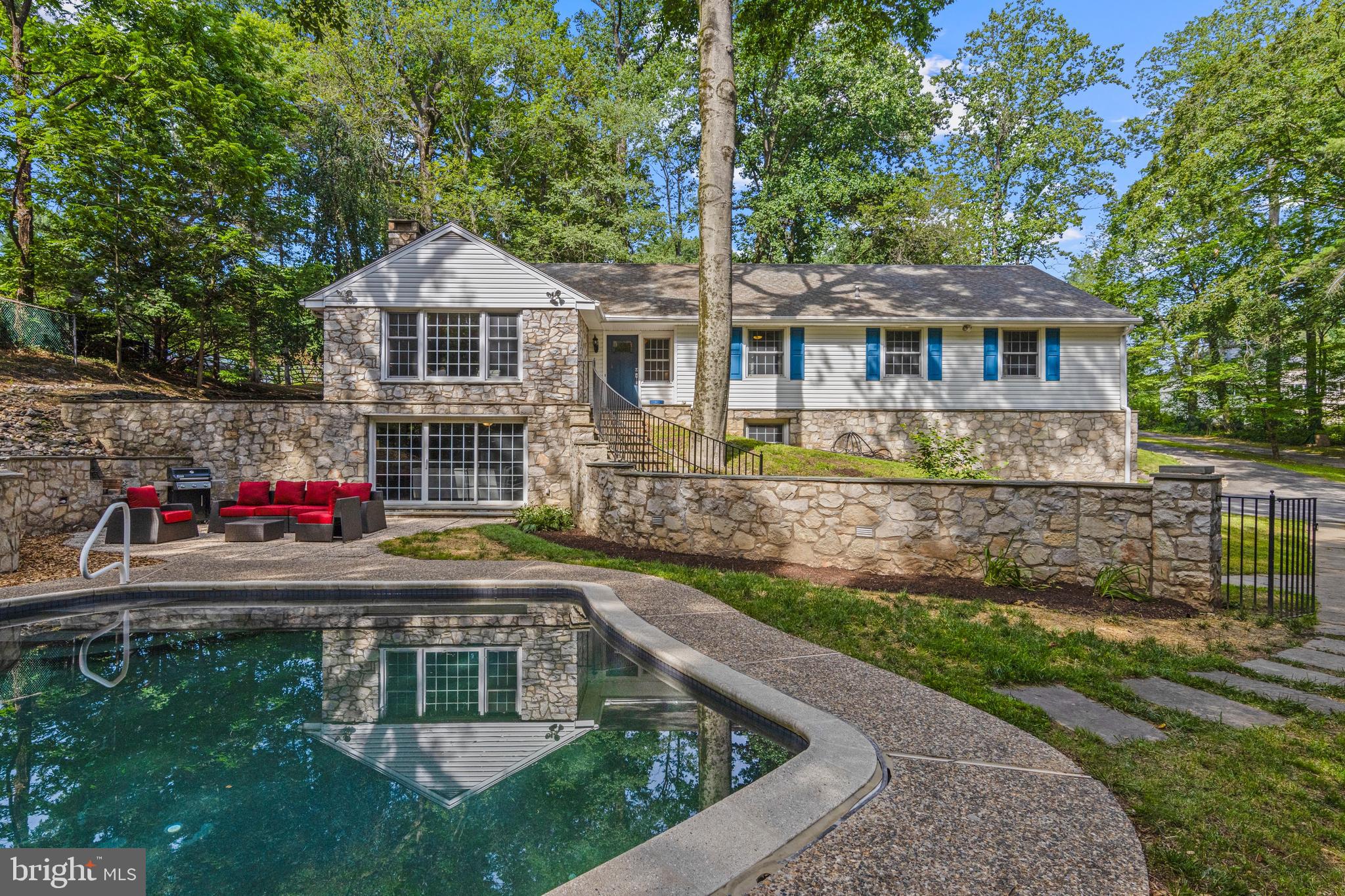 Set on a cul-de-sac in a peaceful, tree-lined neighborhood, 13 Weirwood Road is a home that effortlessly combines privacy, space, and thoughtful updates. With just under an acre of landscaped grounds, an in-ground pool, and an ideal layout for both entertaining and everyday living, this 5 bedroom, 3.5 bathroom home in Radnor Township School District checks every box.
Step inside to find bright, welcoming interiors that flow beautifully from one space to the next. The foyer offers a stylish entry with slate flooring and access to both the living/entertaining areas to the left and the more secluded bedroom wing to the right. The living room is spacious and full of light, featuring hardwood floors, expansive windows with pool views, and a stunning stone fireplace. It opens to the heart of the home: a wide-open kitchen and dining area through with plenty of room to host large dinner parties. The updated kitchen features custom white cabinetry, a striking navy island, granite countertops, and top-tier appliances—including a 5-burner cooktop, double wall oven, and counter-depth refrigerator. A vaulted ceiling and oversized windows provide a dramatic view of the backyard and bathe the space in natural light. Off the kitchen, a generous dining and family room area features new flooring, custom built-ins, and sliding doors that open to one of the outdoor patios—ideal for dining al fresco or simply relaxing by the pool. The backyard includes garden beds and plenty of room to run and explore. A private hallway leads to four well-sized bedrooms, including a serene primary suite with two closets and a beautifully updated en suite bath complete with radiant-heated tile floors and a tub with glass door. Two more full baths and a stylish powder room serve this wing. Downstairs, the fully finished lower level offers tremendous flexibility with a large open living space, custom built-ins, a wet bar with fridge, a cozy gas fireplace, and direct access to the pool patio. A fifth bedroom and full bath ensuite on this level make it the perfect guest suite, in-law space, or teen/college retreat. Additional highlights include a 2-car attached garage, mudroom entrance, tons of storage space. This beautiful private home in a fantastic neighborhood with on a cul-de-sac is perfect for walking and biking. This is a home where every season feels like a getaway.