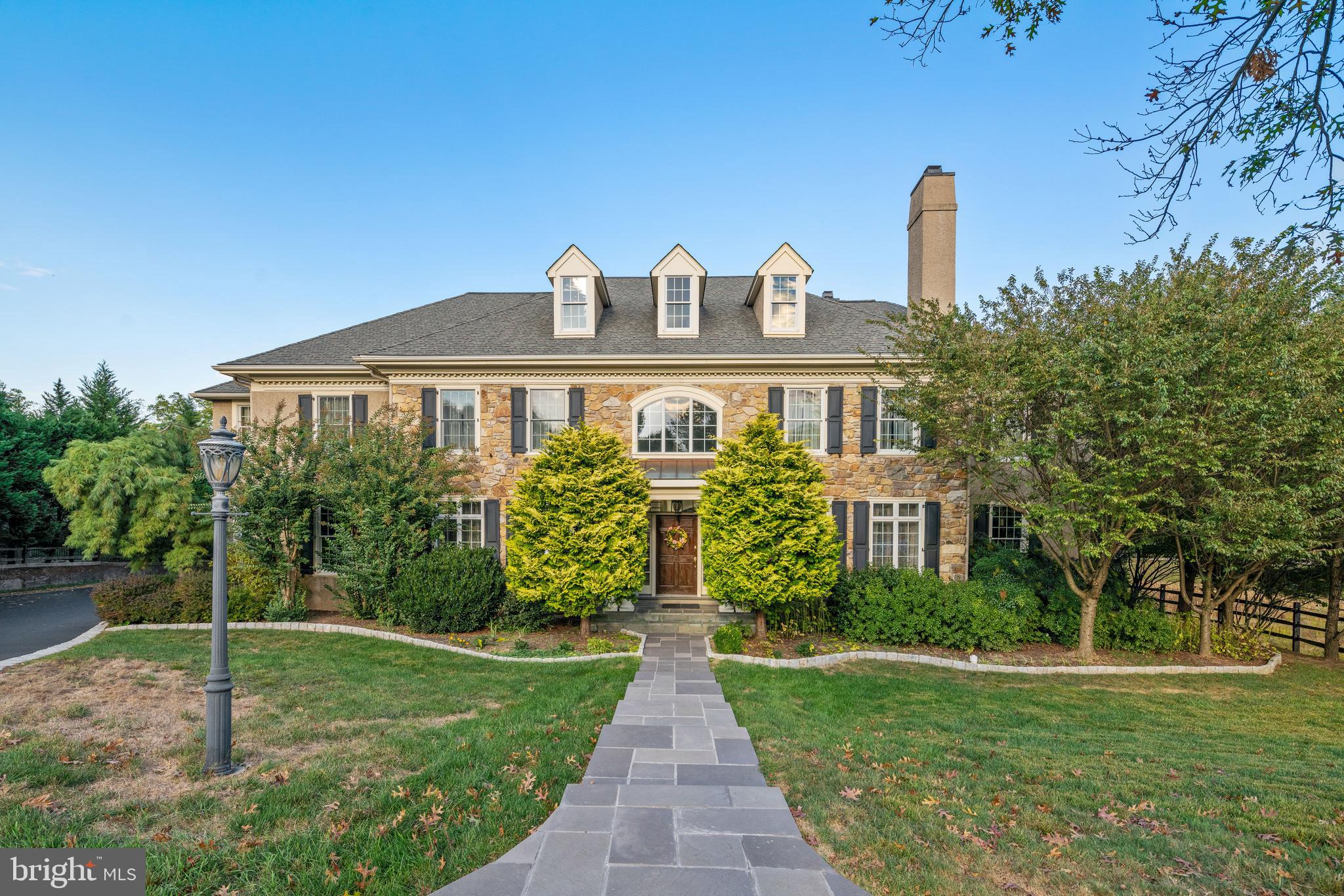 Nestled on sprawling park-like grounds in a premier locale in Wayne rests this grand stone colonial designed for modern family living. Expansive interiors are complemented by a large rear deck and enormous level backyard for exceptional indoor-outdoor entertaining. A double-height entry enriched by hardwood floors reflects the elegance and comfort afforded by this gracious home. Proceed through a wide opening to lounge in the light-filled formal living room with a cozy fireplace. Tall glass-paneled doors lead outside and bring nature’s beauty in. A tasteful dining room sits across the center hall creates a seamless flow for hosting, with its own glass doors to a covered patio. The spacious, sunny kitchen is the heart of the house centered by a massive island that is perfect for appetizers, buffet-style meals, or guests and family hanging out while the cook creates. Chefs quarters are finely appointed with abundant wood cabinetry, granite countertops, and premium stainless steel appliances. A wonderful vaulted breakfast room adjoins, surrounded by triple walls of windows framing scenic property views. Take your coffee or snacks out to the peaceful deck through French doors where you can also enjoy grilling all summer long! By the kitchen is a convenient side entrance with powder room, sizable closets, and easy access to the attached 3-car garage. The piece de resistance is the dramatic yet inviting family room, likely to be your very favorite gathering place, with soaring ceilings, a striking floor-to-ceiling stone gas fireplace, and huge arched windows above sets of French doors to the outdoor patio. A private office with patio access provides a quiet spot for working remotely. The upstairs bedroom level greets you with an airy open landing and presents 5 generous bedrooms beyond. Relax in your serene primary bedroom marked by a lovely recessed ceiling, 2 big walk-in closets, and a sitting area with French doors to a delightful balcony. The gigantic en-suite primary bath pampers with a soothing soaking tub, oversized shower, double sink vanity, and separate water closet. You’ll also find 2 additional bedrooms suites, 2 bedrooms sharing a Jack & Jill bath, and a laundry room on this floor. For the most fabulous parties, events, and celebrations for all ages, the colossal basement is fit for any occasion. It offers a fantastic open rec room with hardwood floors, a half bath and full bar that is like having your own catering or dance hall! Plus there’s tons of storage space and unlimited possibilities for all your needs.