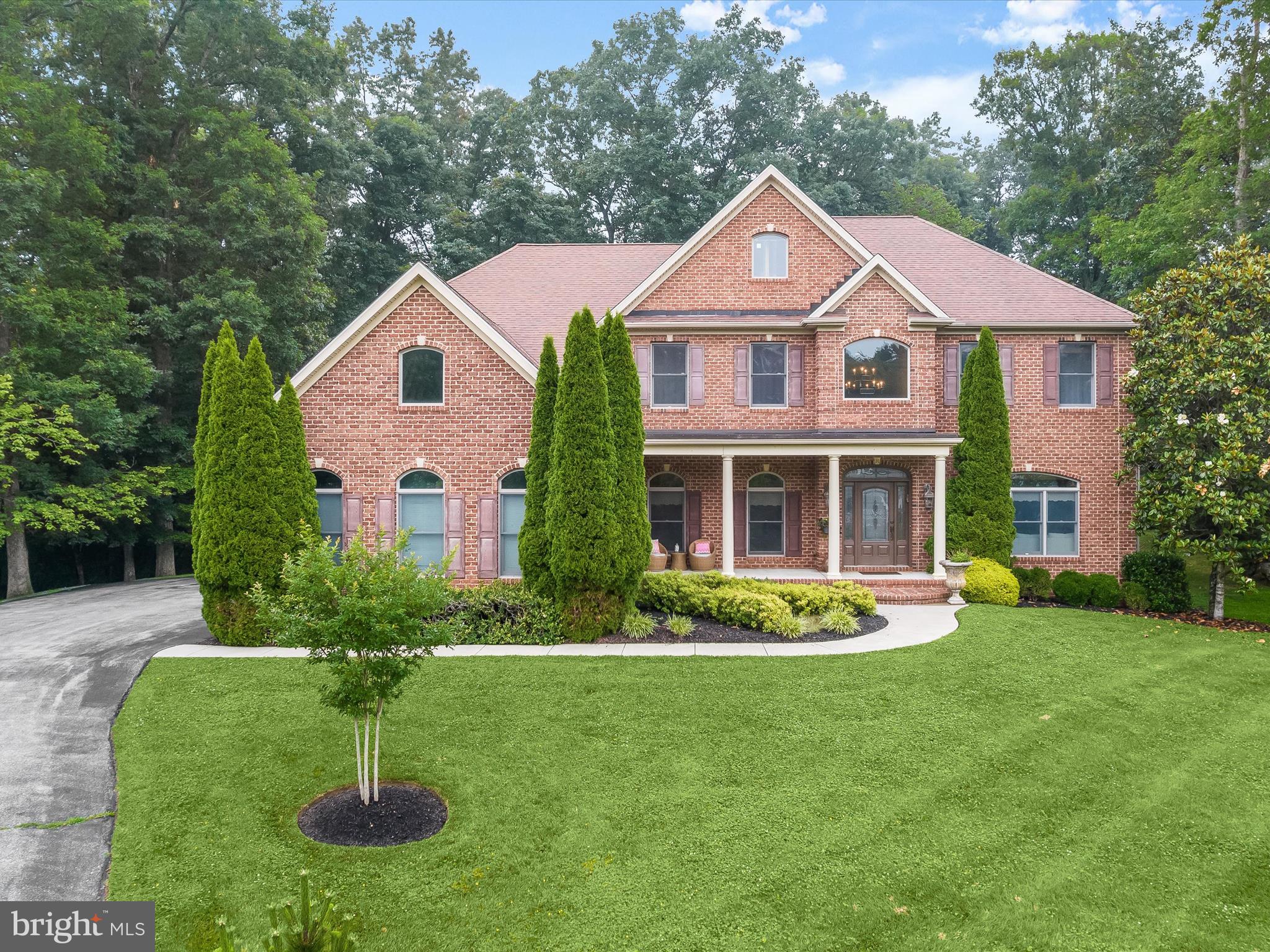 Refined and inviting, this exquisite five bedroom, four and a half bathroom home sits tucked at the end of a tranquil cul‑de‑sac on a stunning 1.18‑acre lot backing to trees. Beautiful landscaping and a covered front porch greet you upon arrival, offering the perfect spot for savoring morning coffee or evening cocktails. Inside, the two-story foyer showcases a wrought-iron staircase and hardwood floors, setting a tone of remarkable craftsmanship echoed throughout with custom millwork, crown molding, and wainscoting. A pair of gracious living and dining rooms flank the foyer, leading through a butler’s pantry into an expansive eat-in kitchen equipped with granite countertops, tile backsplash, an island, underlit 42-inch cabinetry, and stainless steel appliances including a double wall oven and gas cooktop. The adjacent breakfast nook features a desk station and walk-in pantry, while the sitting room provides a casual lounge space. The inviting family room, complete with a gas fireplace, beckons relaxation. On the main level, a versatile fifth bedroom with a cathedral ceiling and outdoor access offers various possibilities as a sunroom, lounge, or playroom. French doors lead into a private office for quiet working or studying. Finishing the main level are a half bathroom and large laundry room with direct entry to the three car garage. Ascend upstairs where the primary suite awaits with a sitting room and two walk-in closets. The luxurious ensuite bathroom boasts a jetted tub, walk-in shower with body sprayers, dual vanities, and a water closet. Across the hall, the second bedroom includes a private ensuite bathroom, while the third and fourth bedrooms share a connecting full bathroom. Downstairs, the fully finished lower level expands the living space and features a massive recreation room for everyone’s activities and entertainment, complete with a bar. A bonus room with a walk-in closet offers potential as another bedroom with an adjacent full bathroom with a walk-in shower. A hobby room adds further flexibility for use as a gym, craft space, playroom, and more. This exceptional home also highlights zoned heating and cooling systems, a three car side entry garage, and a long driveway providing plentiful parking.