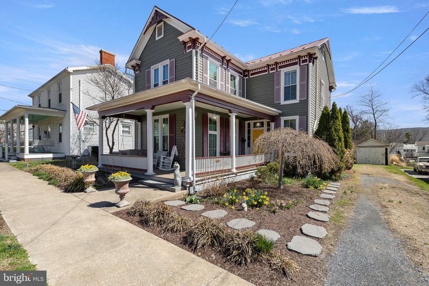 Travel down this tree-lined street reminiscent of years past, when the homes were elegant and grand and everyone could be found conversing from their front porch.  Woodstock is still much of that same town, where you’ll find people walking their dogs and pushing strollers, enjoying small town living.   Located just a short walk downtown where you can grab a burger and beer, take in a Sunday matinee, and enjoy parades and street festivals year round. This lovely Victorian greets you with it’s bold and commanding presence softened by perennial plantings for 4 seasons of beauty. A cheery original, ornate yellow door bids you welcome.  Once inside, you’ll find that this home has been lovingly updated without compromising it’s beautiful character and charm.  Original entrance columns, nine foot ceilings, hardwood floors, transoms over interior doors, lots of built-ins and a sweeping staircase are just a few of the quality features.   Sunshine filters in through large windows and gas logs offer a cozy den to relax at the end of the day.  A new and functional kitchen with upgraded counters, custom built cabinetry, massive island space and modern appliances are a cook’s dream.  The dining room will easily seat an extended table and is tastefully decorated with wallpaper from days past.  Showcase your treasured dishes in the built in cabinetry.   The main level also includes the front parlor or the perfect at home office with custom built-in bookcases.   A bath has been added for convenience to this main level.   On the upper level you’ll find 4 bedrooms, full bathroom and laundry, plus those winding back stairs that are a shortcut to the kitchen.  Did I mention the stairs to the attic?  Use as storage or finish off for more living space!  There’s even more to enjoy- stepping into the screened porch with hookups ready for a hot tub, and ample sized deck cut around a live tree offering shade during the summer.  A detached garage, great for housing the mower or extra storage and private driveway are additional features.
The partially fenced back yard offers both privacy and open space, including two raised garden beds ready for spring planting.  The major components of this home have been updated such as vinyl siding, windows, HVAC system, and freshly painted roof and gingerbread trim.   So make your move in 2026!  Take in the scenic mountains and breathe in the country air, it’s waiting here for you.