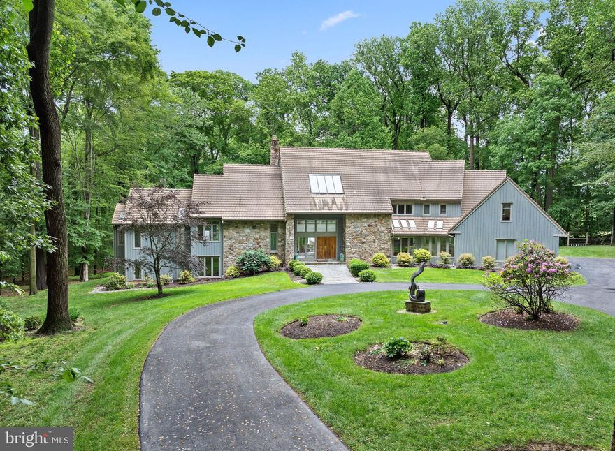 Nestled in the heart of Willistown Township’s coveted Radnor Hunt country, this extraordinary contemporary home blends modern luxury with breathtaking natural surroundings. Set  on 6 private acres, backing to White Manor Country club’s golf course, this light-filled retreat offers unparalleled design, comfort, and versatility. At the end of a cul de sac and down the long tree lined drive past the secondary living structure, currently utilized as an art studio, this stunning home in the most private setting awaits.
Walls of glass and soaring ceilings invite the outdoors in, creating seamless transitions between expansive interior spaces and the breathtaking environment beyond. As you enter the home you are greeted by a gracious fountain, and sunlight streaming through into the open and airy living spaces. The living room—with its sleek fireplace, wet bar, and panoramic views—anchors the open floor plan. A gourmet chef’s kitchen is open to a family room and breakfast room featuring modern lacquer cabinetry, high end stainless appliances and black countertops opens effortlessly to multiple living and dining areas, both indoors and out. 
A few steps up  is the expansive primary suite, a sanctuary unto itself, complete with a sitting room with fireplace, private deck, dual walk-in closets, and a spa-like en suite bath. Upstairs, the open hallway takes you to the three spacious bedrooms each with generous closet space, including one with an en suite bath and two that share a Jack and Jill bath—perfect for family or guests.
A private in-law or nanny suite, situated away from the main living area, with its own staircase offers its own bedroom, full bath, and sitting room tucked away for privacy.
The walkout lower level is a destination of its own—featuring a private home office, spacious family room, a recreation room with wet bar, gym, full bath, and a rejuvenating sauna.
A main floor laundry room, large mud room, 2 powder rooms, a 3 car garage and a large unfinished storage area are just a few of the additional highlights of this home. 
Outside, the grounds are nothing short of spectacular. Enjoy a series of beautifully designed outdoor living spaces, from flagstone patios to lounging terraces surrounding the sparkling pool. Multiple dining areas are nestled under a canopy of trees and framed by seasonal blooms, while the professionally landscaped gardens showcase rare and mature specimen plantings throughout the property. A freestanding art studio with its own half bath offers endless possibilities as a creative retreat or guest escape.
This exceptional property blends contemporary architecture with the timeless appeal of Pennsylvania’s countryside—offering complete privacy, refined design, and close proximity to the Main Line’s finest schools, shops, and dining.
This is a rare opportunity to own a one-of-a-kind contemporary estate in one of the Main Line’s most picturesque and prestigious settings.