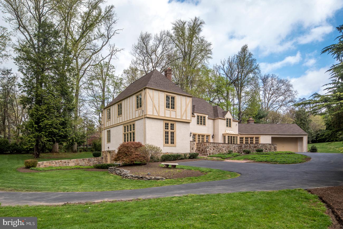 Truly stunning and very expansive, this grand Tudor home is a beautiful expression of light, airiness and elegance, with a gracious flow for entertaining. It is desirably located in the prime, picturesque estate section of Northside Villanova, on nearly 1.5 +/- impeccably landscaped acres, near top Lower Merion schools and a host of conveniences for the entire family. A circular drive, lush private grounds, and a gorgeous exterior with stone accents and new roof create curb appeal galore. In front, a spacious brick paver patio provides a perfect setting for enjoying the blissful views. The breathtaking interior is bathed in natural light and brimming with lots of wonderful architectural features. Every detail and room is distinctive, beginning with the inviting foyer beyond arched wood doors, making an instant impression with a striking staircase, rich hardwood floors, and open views of the sunny 2nd floor landing. Coat closets and a powder room sit conveniently off the foyer. At left through an arched opening awaits a large and lovely step-down living room with generous front-facing windows overlooking greenery and a charming wood-burning fireplace. Also nearby is a library/den with custom built-ins and serene rear property views. A gallery leads to the formal dining room with chair rail moldings and French doors opening to the patio, affording a seamless connection between the in/outdoors, heightening the experience for special occasions and everyday living. Adjacent is a white eat in kitchen where the hardwood floors continue and family/guests converge. A huge tiered island with seating and granite tops, abundant cabinetry and prep space, stainless steel appliances, and a divine open breakfast room awash with light make this the heart of the home. Adjoining is a fabulous family room where you can relax with loved ones, boasting high vaulted ceilings, a second wood-burning fireplace, and more French doors spilling out to the patio. The main stairs ascend to an open upper landing making way to 4 comfortable, well-proportioned bedrooms. Unwind in the room master retreat occupying one wing, with plush carpeting, vaulted ceiling, a walk-in closet, and en-suite marble master bath with a jetted tub and separate shower. The additional 3 bedrooms share 2 full hall baths. A walkout basement, 2-car garage, and sprawling lawn for the kids and pets round out the good life!