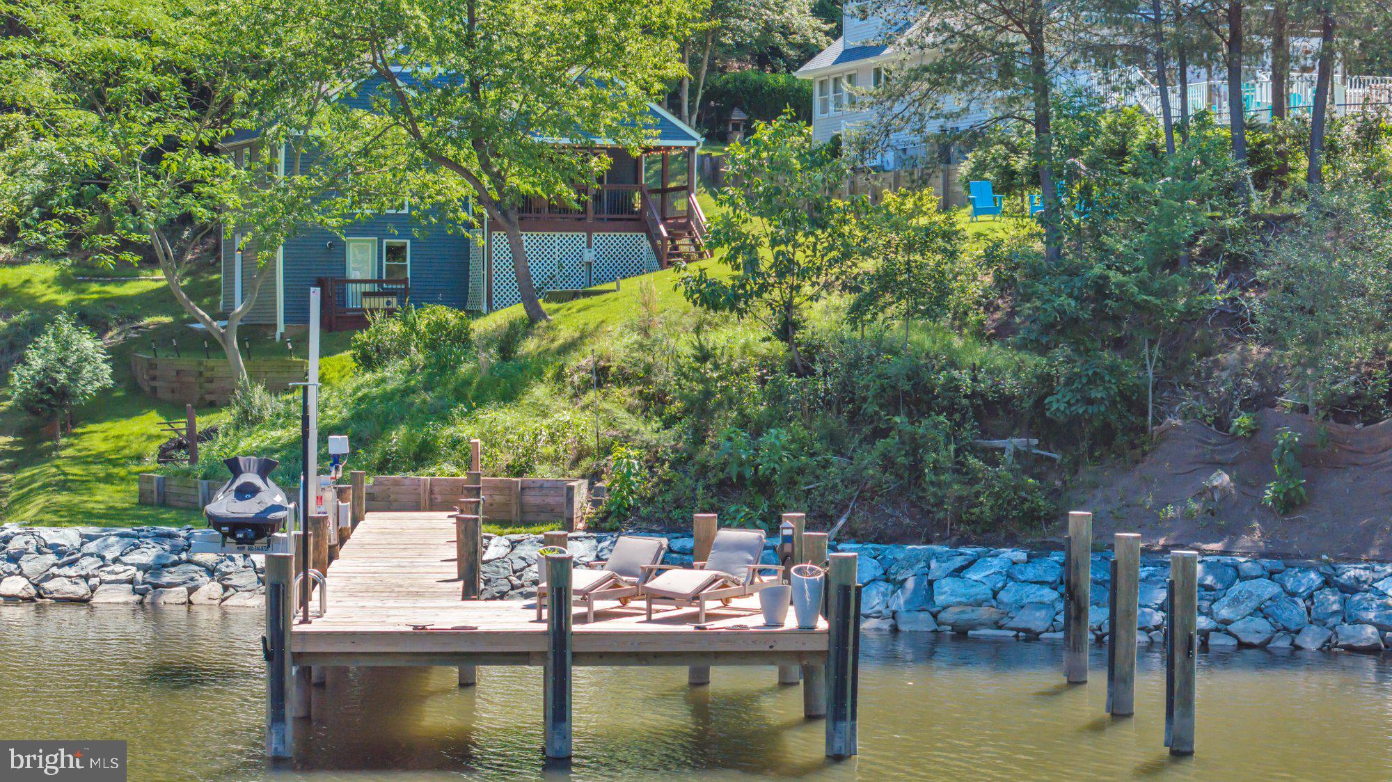 A serene and secluded waterfront escape awaits you on Mathias Cove in Forest Glen.  This one will steal your heart the second you walk in the door. The beautifully renovated kitchen opens to a great room with vaulted ceilings, great natural light and hardwood floors throughout the main level. Large sliding glass doors expand your gathering space to a huge covered deck overlooking the water, a perfect place for dining or relaxing with a book on a summer day.  The kitchen features classic shaker style cabinetry, stainless steel appliances and lovely granite countertops. Great decorative elements include subway tile backsplash, floating wood shelves, and shiplap surround for the eat-in breakfast bar. A cohesive color scheme and smart home Lutron lighting continue throughout the home. The open living and dining area allows for flexibility in the main living space, and the covered deck can easily accommodate both lounge seating and dining. The primary bedroom overlooks the water through an oversized picture window, providing the perfect morning view. Paired bedroom closets provide plenty of storage.  An attached primary bathroom features a fully tiled walk in shower and updated fixtures. The main level also features a second bedroom, and a full bathroom with gorgeous tile and finishes. The lower level family room has built-ins and a wall mounted television, and provides direct access to the back yard and waterfront as well. A utility room on the lower level was updated by the current owners who added a work sink and a front loading washer & dryer to the home. Many other home improvements are detailed on the Property Information Sheet included with the property brochure and disclosures.
This property is truly unique, and all about enjoying the waterfront lifestyle on the Chesapeake Bay. In the summer of 2024, the homeowners completed an extensive shoreline restoration in collaboration with their landscape architect, featuring hand-laid boulders that stabilize and beautify the shoreline. At the same time, a completely rebuilt pier was finished, offering deep water access for all your boating needs. The pier includes fresh pilings, updated decking and a large slip, along with the addition of electricity and plumbing, feature previously unavailable at the waterfront. The dock features 100am service with a custom pedestal from International Dock. A High Tide Jet Ski lift with 15 amp service was also installed, along with three new water bibs. Custom Humberton Forge lighting complete with a Lutron timer system lights up the pier at sunset. The home is also equipped with a French drain system for effective water management. Additional Landscape site plans already completed are available for review and will convey with the property.
This is an opportunity to purchase a unique waterfront property where high quality work for all your boating needs have already been completed. Just move in and start living the waterfront dream!