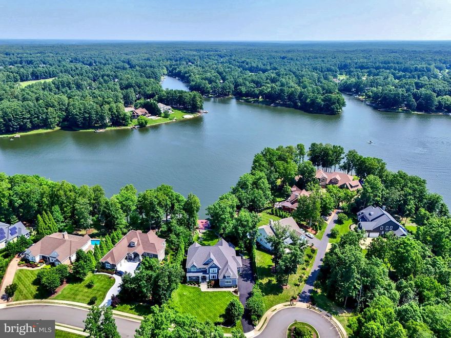 The epitome of waterfront living, this exceptional luxury Dream Home is located within Fawn Lake, one of Virginia's most prestigious gated resort-style communities. Meticulously blending classic Hamptons style elegance with timeless architectural details, this masterpiece crafted by renowned builder, Simply Homes, spans an impressive 10,000+ sq ft on three levels of well-appointed living space with premium amenities and a setting that is both peaceful and breathtaking. Perched on a beautifully landscaped lot with manicured grounds offering dramatic views of the water, this residence provides an unparalleled combination of privacy, luxury, and tranquility, capturing the essence of coastal lakeside charm. Embracing the allure of waterfront living in all its splendor, this extraordinary home delivers effortless flow across open, light-filled spaces oriented to maximize panoramic water views. Setting the tone for a refined waterfront lifestyle, where comfort and elegance meet in perfect harmony.  The coastal modern interior features a thoughtfully designed floor plan that balances open, airy common spaces with quiet retreats. Built with an elevated eye for design, this home features high-end upgrades and custom finishes throughout. A soaring two-story foyer sets the tone from the moment you step through the door, flowing into a dramatic Great Room with a wall of glass doors that frame backyard views and fill the space with natural light. An elegant Living Room features expansive windows that flood the space with natural light and offer amazing views of nature.  The Great Room with 10 ft coffered ceilings is anchored by a stunning fireplace and media cabinetry,  creating a warm and inviting atmosphere. Massive  Andersen sliding doors offer seamless access to the lakeside covered porch, providing some of the most breathtaking water views in Fawn Lake.  The show stopping Gourmet Chef's Kitchen, equipped with top-of-the-line appliances, custom cabinetry, quartz countertops, a massive center island and an amazing Scullery pantry caters effortlessly to both intimate family living and grand-scale entertaining. The adjacent light-filled breakfast area with large windows boasts spectacular water views. With access from the kitchen and great room, a stylish butler's pantry and wet bar leads to the formal Dining Room, perfect for casual family meals to elegant entertaining.  An inviting sunlight Den with vaulted beamed ceilings and incredible views of nature, offers a tranquil versatile space.  A true  sanctuary, the main floor Primary Suite features a luxurious spa bath including a marble tile shower, soaking tub, and a fabulous closet.  This level is complete with an amazing Keeping Room, featuring a built-in office desk, drop zone, storage cabinets, and laundry area! The upper level includes Three generously sized bedrooms with ensuite baths, each thoughtfully designed with style and privacy in mind. Plus an oversized Bonus Room. The expansive lower level with stunning lake views, offers plenty of entertainment and leisure  options. Including a Rec Room,  Game Lounge, Gym, Kitchenette, and additional Bedroom with ensuite Bath. Outdoor living is equally impressive, with resort-style amenities highlighted by an inviting Veranda with built-in BBQ, dining space and lounging area with fireplace for cool summer evenings. An oversized covered porch and flagstone patio on the lower level are perfect for outdoor living.  A sweeping lawn with terraced walkway leads to the water's edge with a stone firepit and  private dock, which offers direct access to boating, fishing  and paddle boarding.  The waterfront setting with ever-changing views and a calming ambiance, provides a perfect backdrop for creating lasting memories. Whether entertaining on a grand scale or enjoying quiet, everyday moments, this extraordinary residence offers an incredible opportunity to embrace the magic of Country Club life and the ultimate waterfront lifestyle at Fawn Lake!