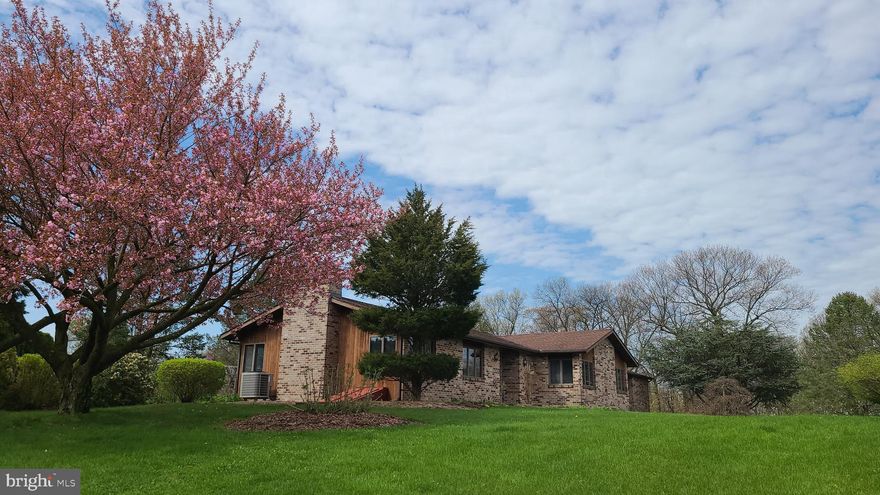 As you approach this lovely brick and cedar home you will start to take in the  views that become all but panoramic.   1080 Mahlon Drive is perched on a gentle rise in scenic Bern Township.  This one owner home was built on a double lot to accommodate the needs and dreams of a young and growing family.  Meticulously kept and improved for the next beneficiary is this expanded ranch style home.  Park outside the two car, side entry, expanded garage and follow the front walk to main entry.  Here you will want to turn and take in the northeastern view of the Schuylkill River Valley and the Blue Mountains beyond (The view is as good or better from the great room ).  Turn again and proceed into the ceramic foyer with ample furniture space and two large closets for storage and convenience.  By now you have been enticed to look if not enter the huge great room that helps define this lovely custom home.
This family friendly room was expanded and upgraded with a floor to ceiling fireplace, wood beam, vaulted  ceiling and three walls with windows to take in the abundance of natural light often a daily presence  on "the hill".  Leaving the great room you enter the well appointed kitchen where views of the artistic back yard start to be appreciated.  This bright, naturally lit kitchen is accompanied by the adjoining dining area with sliding door to the rear 12' x 24' covered patio.  To save the rear yard tour for last, you can explore the rear hall with main level laundry facilities and access to the expanded, high ceiling garage.  Leaving the dining area toward the front hall we proceed to the bedroom hallway with two bedrooms to the front and the primary bedroom straight ahead.  Double lighted closets abound in the bedrooms for plenty of storage and convenience.  The main bedroom bath has a whirlpool tub for those relaxing needs in our busy lives.  Now, let us go to the rear yard where one will spend countless hours as the sun sets and the cool of the evening enhances the  peace and quiet to this secluded haven.  The present owner has transformed the rear lawn into an artist's canvas, with natural elements to attract birds, and provide herbs and vegetables for the dinner table.  To add to the comfort, efficiency  and security of this rural suburban home there is a 2' x 6' construction, a backup generator,  advanced  water treatment systems and if needed school bus pick-up in the neighborhood.  This sale is contingent on Seller's purchasing their daughter's home. They will require a lease back for a short time.