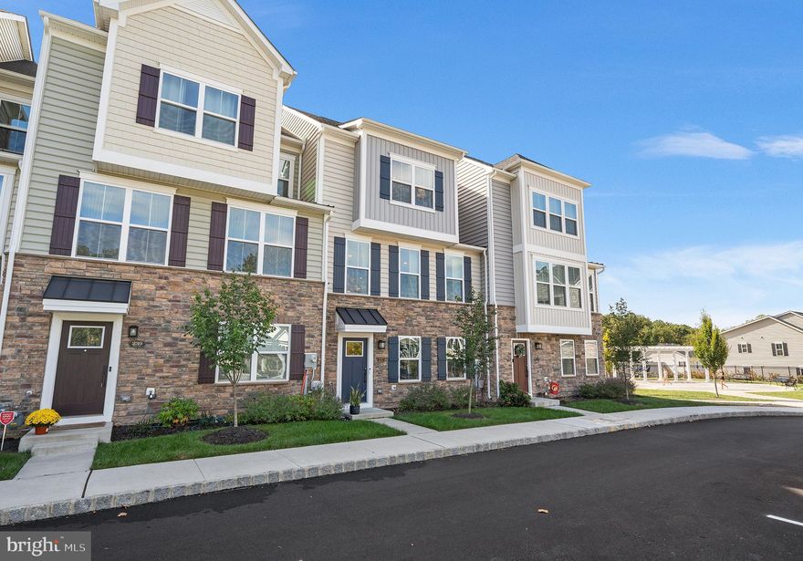 Nestled in the sought-after Ponds Edge community, just four miles from vibrant downtown Media, this nearly new stone-front townhome blends sophisticated design with seamless, inviting spaces. Thoughtful details shine throughout, from soaring nine-foot ceilings to hardwood floors, designer lighting and an open, light-filled layout. The entry level features a bright home office with French doors for privacy, mudroom with built-in bench and convenient access to the attached two-car garage. Upstairs, the open-concept main level is an entertainer’s dream—a chef’s kitchen with quartz countertops, oversized island with seating and gleaming tile backsplash flows seamlessly into the dining area and spacious great room. Step through glass sliders to the covered porch with gas fireplace, stunning stone accent wall and space for a TV—the perfect spot for year-round gatherings and cozy nights at home. A powder room completes this level. Upstairs, two secondary bedrooms share a full hall bath, while the sumptuous primary suite boasts a tray ceiling, custom walk-in closet and ensuite full bath with dual vanities and luxurious double shower. A convenient laundry closet is tucked off the hallway. Outside, sidewalks lead to playgrounds, a fitness center and community clubhouse. Located within the award-winning Rose Tree Media School District and minutes from downtown Media and Septa’s newer Wawa station, this turnkey gem combines upscale comfort with unrivaled convenience.