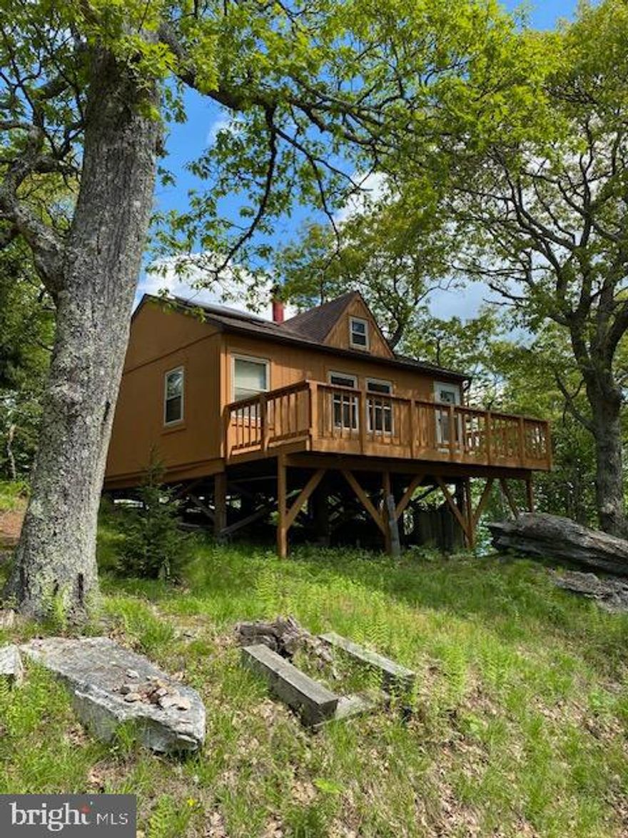 The cabin sits on 8.26 acres of land and is recorded as Tract #1.  There is deeded non-exclusive access to a 9.48 acre Common Area for the development that includes Kile Knob proper and the hiking trail.  That tract is adjacent to Tract #1.  This makes the property feel much bigger and access to the grand views from Kile Knob are a brief walk. The private driveway winds up the property to the cabin. 

 A tall multi rock formation near the Kile Knob Trail marks the Western boundary.  There are two stakes near the driveway entrance that mark the Southern boundary.  The only neighbors green bunkhouse is near the East property stake near an evergreen.  From the Southern boundary, the property stretches out like a baseball diamond.  In the Southern lowlands of the property between the cabin and the driveway entrance is a  flat meadow that deer like to walk through and the owner has set up a modest walking trail down to it. Great area for a firepit and roasting marshmallows. The driveway itself is a hiking asset that completes an enjoyable hiking loop when combined with the Kile Knob hiking trail and deer path that goes by the shed.  The shed houses the electric inverter, has a separate room for batteries, and has plenty of room left over for tools and storage.  The South Facing deck has a propane gas grill and picnic table.  The mature Oaks that anchor three of the four corners of the house provide fantastic shade in the Summer.  The North facing deck has great views of the valley.  Tree-work was performed to enhance the views.  It was decided by the owner to keep the large red spruce in the foreground and hemlock as you look Northwest.  

Electric-  The house has a top-of-the-line Magnum inverter located in the shed.  The batteries have not had any issues and have never failed.  The power is supplied strictly via solar panels on the roof of the cabin.  
Heating- The cast iron stove provides great heat on cold nights.  The dampers allow for slow controlled burns to keep wood burning long into the night.  
Water-  Owners always brought their own water to the cabin.  There was at one time working water at the cabin.  Gutters collect rainwater and feed a cistern above the driveway.   A small blue pump in the utility closet provided the pressure to the shower and the sink in the bathroom.  A tankless water heater was connected to the LP tanks under the house.  In theory there could be running water, but we never used it enough to make it worth the effort to maintain.  Garth got the tankless water heater working at one time.  The kitchen area is plumbed for water, but there is no sink or faucet, but that could be added. The shower was used sparingly but on occasion a battery-operated pump and shower head were used in conjunction with a bucket of hot water. The cabin has a composting toilet.