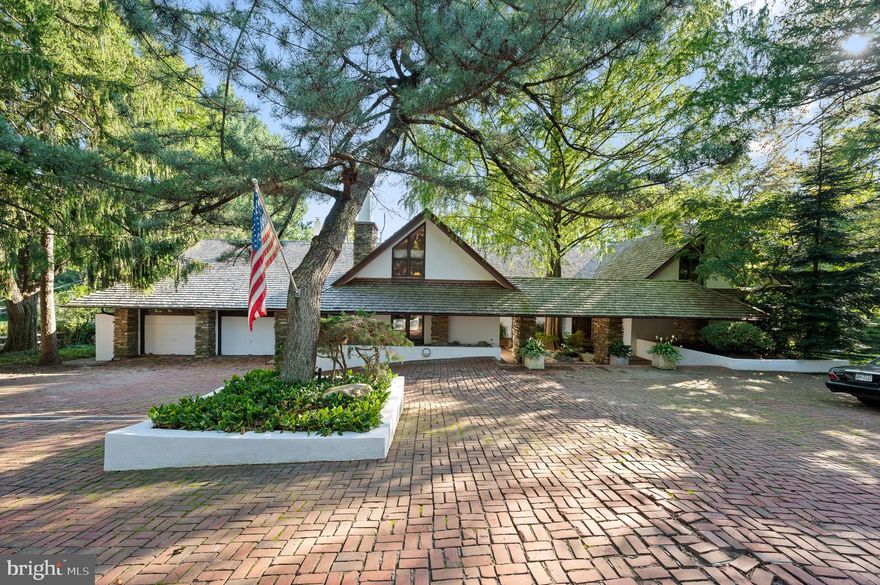The Green House, 1660 Cloverly Lane in Rydal, was designed in 1964 by Malcolm Wells, the father of environmentally responsible design.
The exterior of the home is surrounded by low stucco and stone walls which create a forecourt with heated brick pavers.  The dramatic cedar shake roof with purposeful overhangs is a defining feature.  Stone piers direct visitors to the front and side entrances.
Upon entering, you are greeted by an extension of the exterior’s motif – brick floors throughout, seamlessly blending the outdoors with the indoors.  The interior design reflects the exceptional elements of the exterior again with the use of stone piers which support exposed wood trusses and strategically stepped levels defining an open floor concept, providing a visual and spatial quality of design rare today.
The interior showcases a marriage of aesthetics and functionality.  Copper cabinets and fireplace surrounds highlight the artistic craftsmanship, while a hand carved wood panel beautifully divides the workspace from the eating area, defined by a cantilevered dining table relating to the exterior and interior overhangs.  Standing on the balcony of the second floor, there is a striking view of the architectural highlights of the first floor.
This residence offers 4/5 bedrooms, ample closets, and captivating views of the lush property.  The layout includes three bedrooms on the upper level and 1-2 on the main level, providing a convenient and versatile living space.  The heart of the home is the kitchen providing foodies with a commercial range, oversized Subzero refrigerator-freezer combination and a substantial griddle.
Entertaining is effortless in this home, with expansive family rooms, one directly connected to the kitchen, sitting rooms and a four-season room extension.  The fully finished basement opens up to a lower-level deck, connecting the indoor and outdoor entertainment areas.  The rear of the property has a generously sized level yard, offering a canvas for outdoor activities and relaxation.
An additional high point of this exceptional property is the oversized pool, complemented by a large hot tub and a beautiful pool house equipped with two full bathrooms and an expansive indoor entertainment area providing the perfect setting for gathering and recreation.
The Green House is a fine example of Mr. Well’s design concepts which are still very relevant today.  For a comprehensive list of the property’s highlights, please refer to the attached addendum.