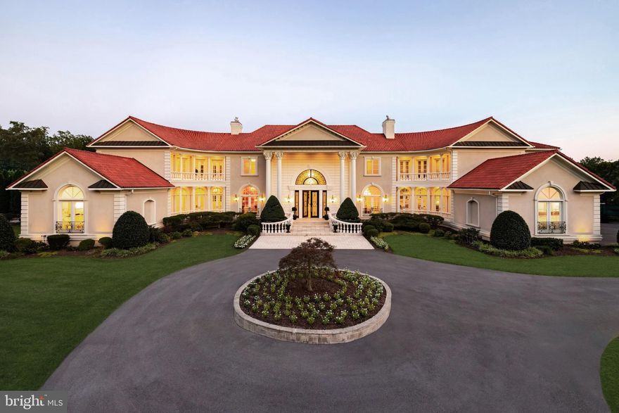 Situated within the coveted enclave of Falconhurst along Potomac’s most distinguished corridor, 9431 Newbridge Drive is a landmark estate that defines timeless sophistication. Conceived by master builder David Niroo and elevated by the artistry of Haleh Design, this residence stands as a testament to classical European architecture, enduring craftsmanship, and uncompromising luxury.

Set on over two private acres and approached through wrought iron gates and a stately circular drive, the home commands immediate presence. Its grand façade is anchored by Corinthian columns, sweeping wings, and a Mediterranean Ludowici tile roof that embody balance, symmetry, and permanence.

Inside, a dramatic 28-foot foyer sets the tone, with twin curved staircases, marble floors inlaid with gold, and a custom chandelier signaling arrival at one of the Capital Region’s finest addresses. Spanning 18,500 square feet, the interiors are both expansive and meticulously appointed. Formal living and dining rooms are designed for entertaining on a grand scale, while intimate spaces such as a paneled library, a sunlit conservatory, and a private main-level suite offer refinement in daily living.

The residence balances elegance with comfort in its informal wing, where a chef’s kitchen with professional-grade appliances and an octagonal breakfast room flow seamlessly into a family gathering space and a five-car garage. Upstairs, two distinct primary suites anchor the level, each with private sitting rooms, dressing salons, and spa baths, complemented by three additional ensuite bedrooms.

The lower level is dedicated to leisure and entertainment. A 46-foot recreation room with a curved wet bar, billiards room, secondary kitchen, home cinema, fitness center with spa bath, and guest accommodations transform the space into a private resort.

Behind the beauty lies engineering of equal caliber. Multi-zone climate systems, tankless water heating, whole-house generators, and advanced security deliver peace of mind and effortless living. Outdoors, manicured grounds, limestone terraces, and architectural lighting create a setting as dramatic by night as it is serene by day.

9431 Newbridge Drive is more than a home. It is a generational estate that offers unmatched scale, provenance, and presence in one of the Capital Region’s most exclusive enclaves.