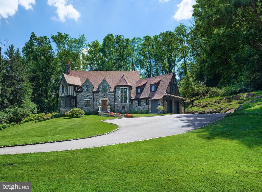 This stunning and stately stone Tudor-style Colonial, designer by Fred Bissinger and hand-crafted by E.B Mahoney, is set  on pristine manicured grounds in Villanova and features gorgeous architectural elements and incredible character. A sweeping driveway welcomes you home and winds to an oversized 2-car garage with peaked roof. The spectacular 1.56-acre property graced by mature trees, lush greenery, beautiful gardens and hardscaping is a breathtaking backdrop for this truly distinctive residence. A lovely flagstone walkway lined with flowers and tasteful lighting brings you closer to the fa ade s exquisite stonework and escorts you to the commanding wood front door. Graciousness and elegance envelop you the moment you step into the entry hall with wood beamed ceiling and stone floors. Beyond awaits a magnificent great room accentuated by airy ceilings, striking exposed wood beams, and open living and dining areas with the stone flooring continuing throughout, affording a perfect flow for entertaining. Relax with company in the light-bathed living room around the fireplace, and sip a cocktail in the charming sitting nook nearby surrounded by windows and showcasing the views. Move seamlessly into the dining room for formal sit-down meals, brightened by a wall of glass with doors leading out to the fabulous paver stone patio and sprawling rear lawn. The cook s kitchen is stylish and functional, with extensive wood cabinetry and pantry space, a huge center island with seating and storage, farmhouse sink, and premium appliances including a stainless Viking 6-burner range, 2nd convection microwave/oven and built-in fridge. Completing this level is a large refined powder room, big laundry room with a 3rd oven, sink and cabinetry, and sun-filled greenhouse room for your favorite plants. Ascending the main staircase of rich wood, a tall window of leaded glass brings light in. The carpeted 2nd story presents 4 bedrooms and 3 full baths for the comfort of family and overnight guests. The vaulted master is exquisite, a private retreat with an oversized arch-top window, 5 fabulous closets, spacious en-suite bath with double sinks, vaulted ceilings, an oversized shower and generous storage. Bedrooms 2 and 3 are bright and well-proportioned, plus there are 2 wonderful tiled hall baths. The huge vaulted 4th bedroom with built-ins is currently used as an office.  Central heating/AC, and easy access to cafes, restaurants, The Philadelphia Country Club, major routes, parks and conveniences further the appeal of this special gem.